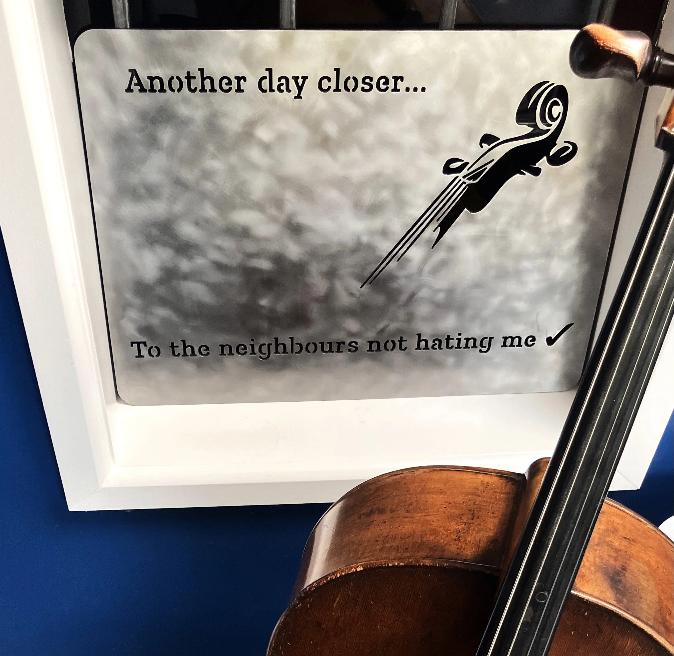 A metal sign with a cello graphic and humorous text that reads 'Another day closer... To the neighbours not hating me'.