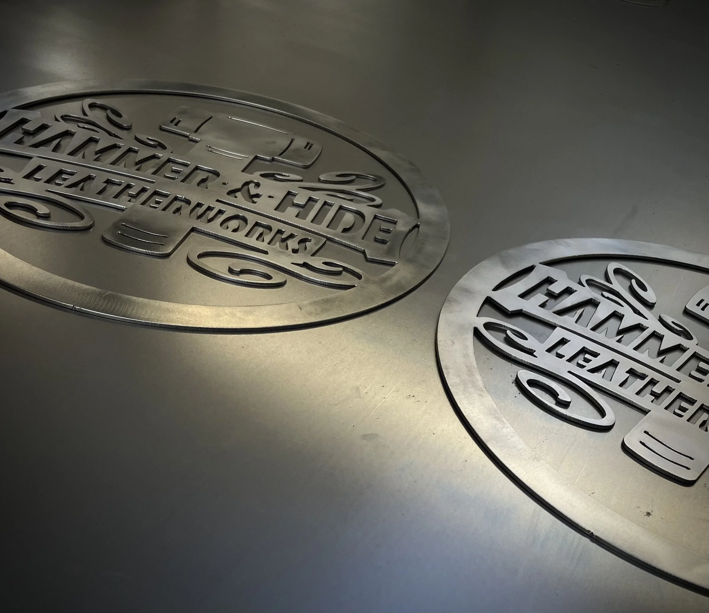 Close-up view of two circular metal plaques with embossed text and designs, placed on a gray surface.