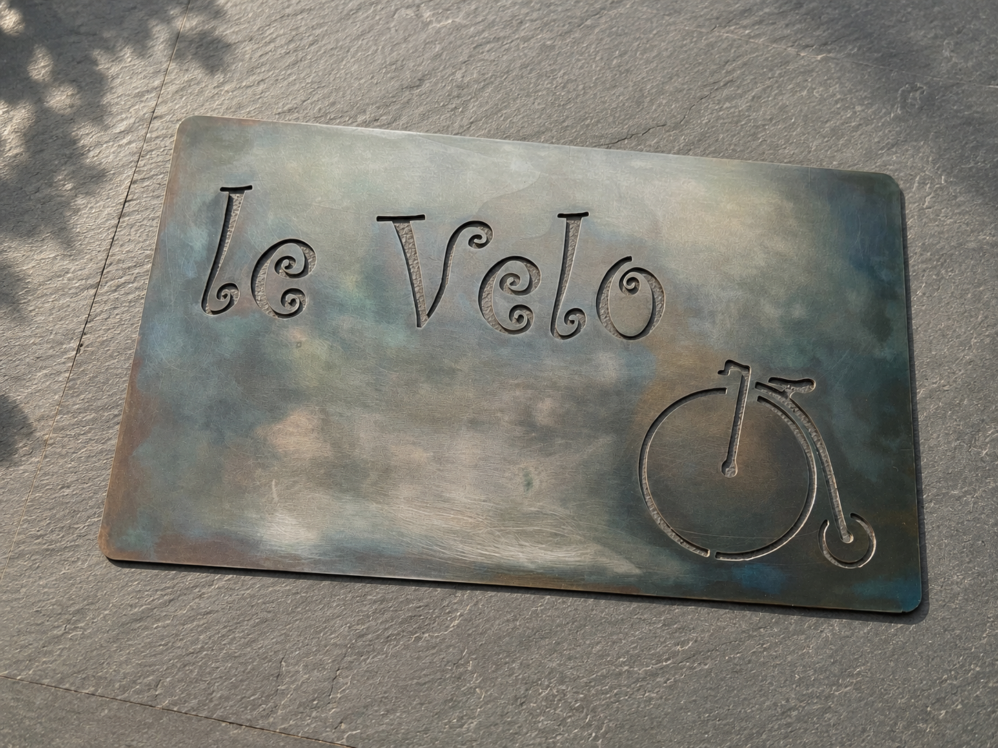 A metal sign with the words "le velo" and a bicycle wheel design, placed on the ground.