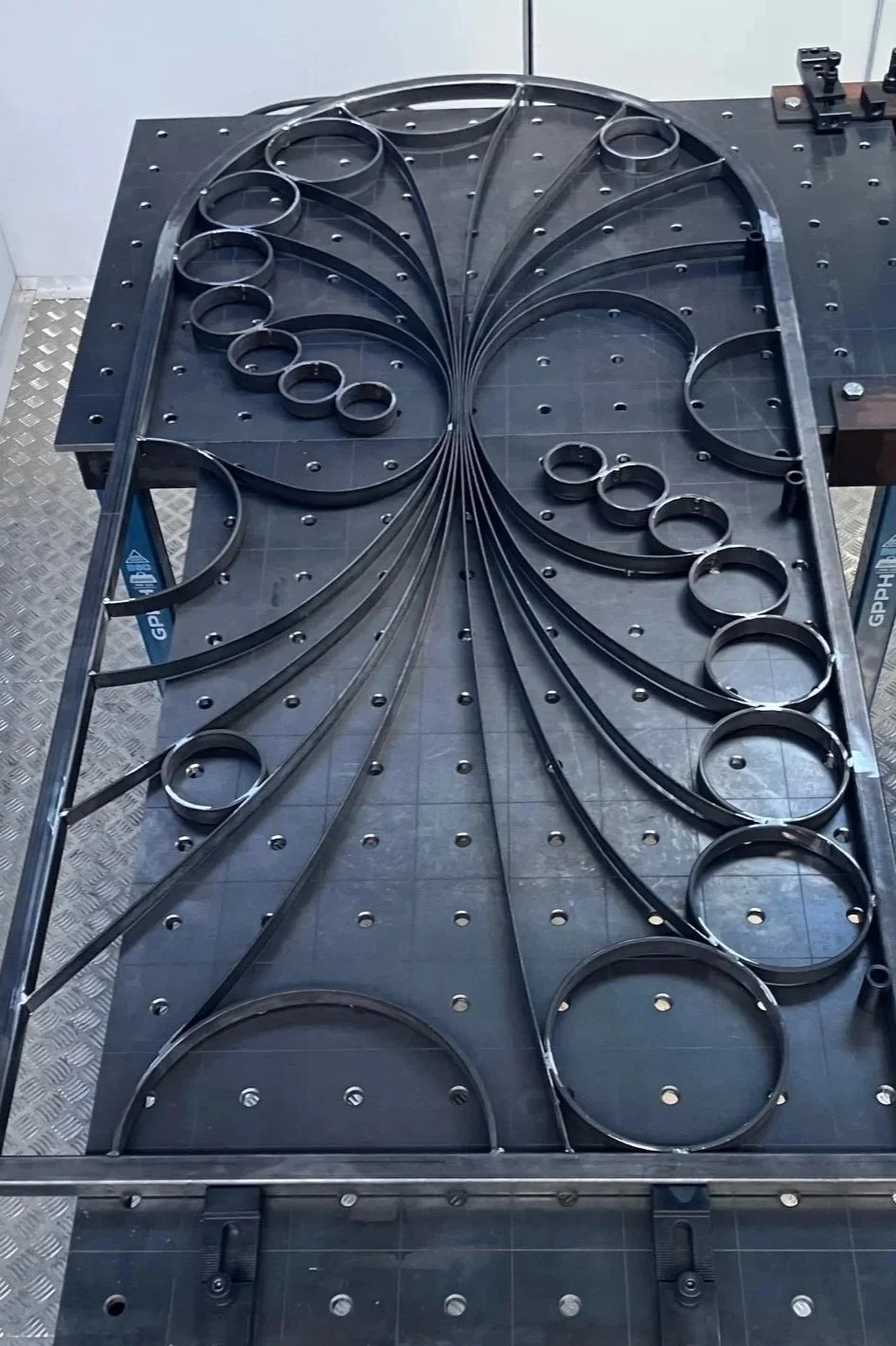 Metalwork on a black perforated worktable with curved metal strips arranged in an intricate pattern.