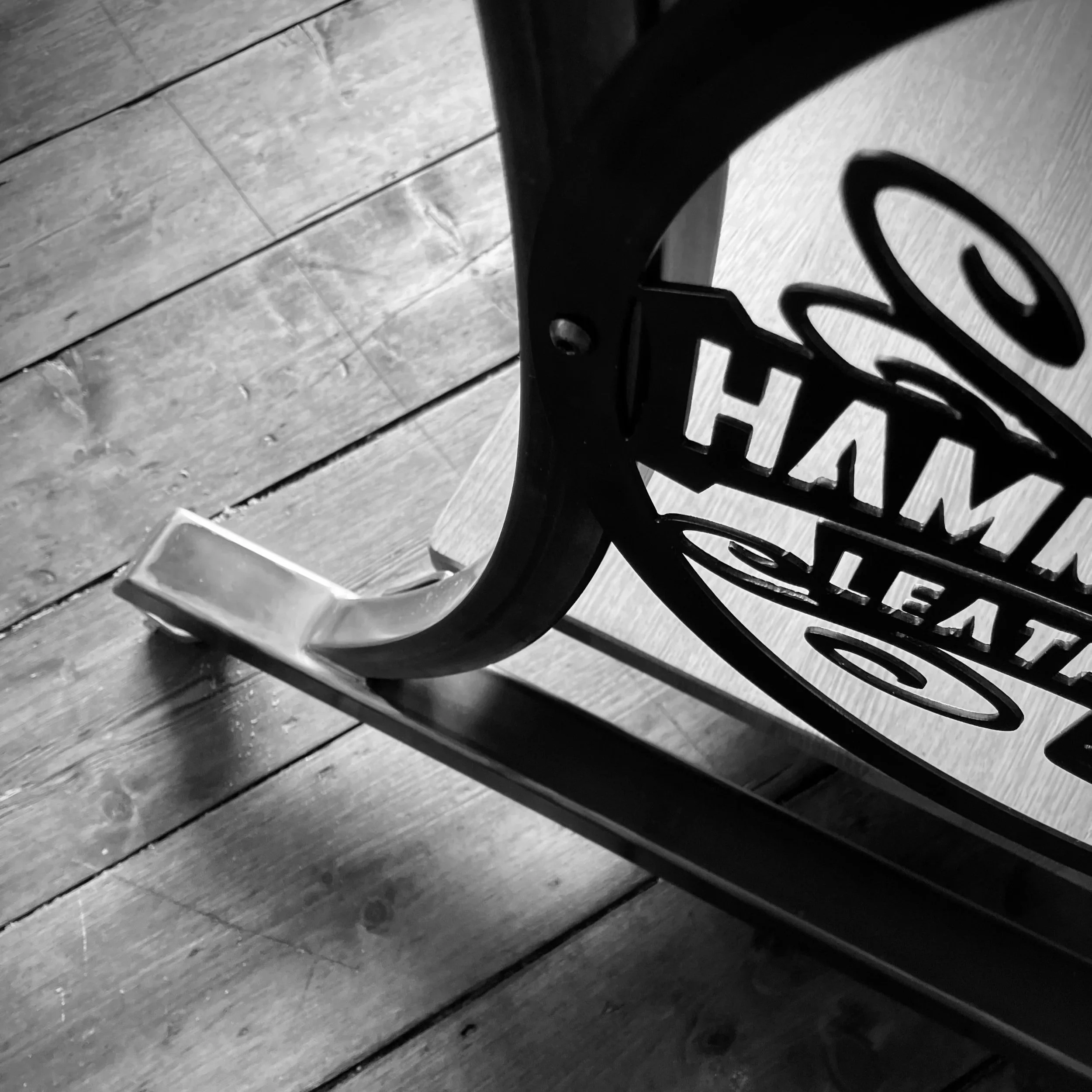 Close-up black-and-white photo of a metal chair or table leg with a decorative cut-out design, on a wooden floor.