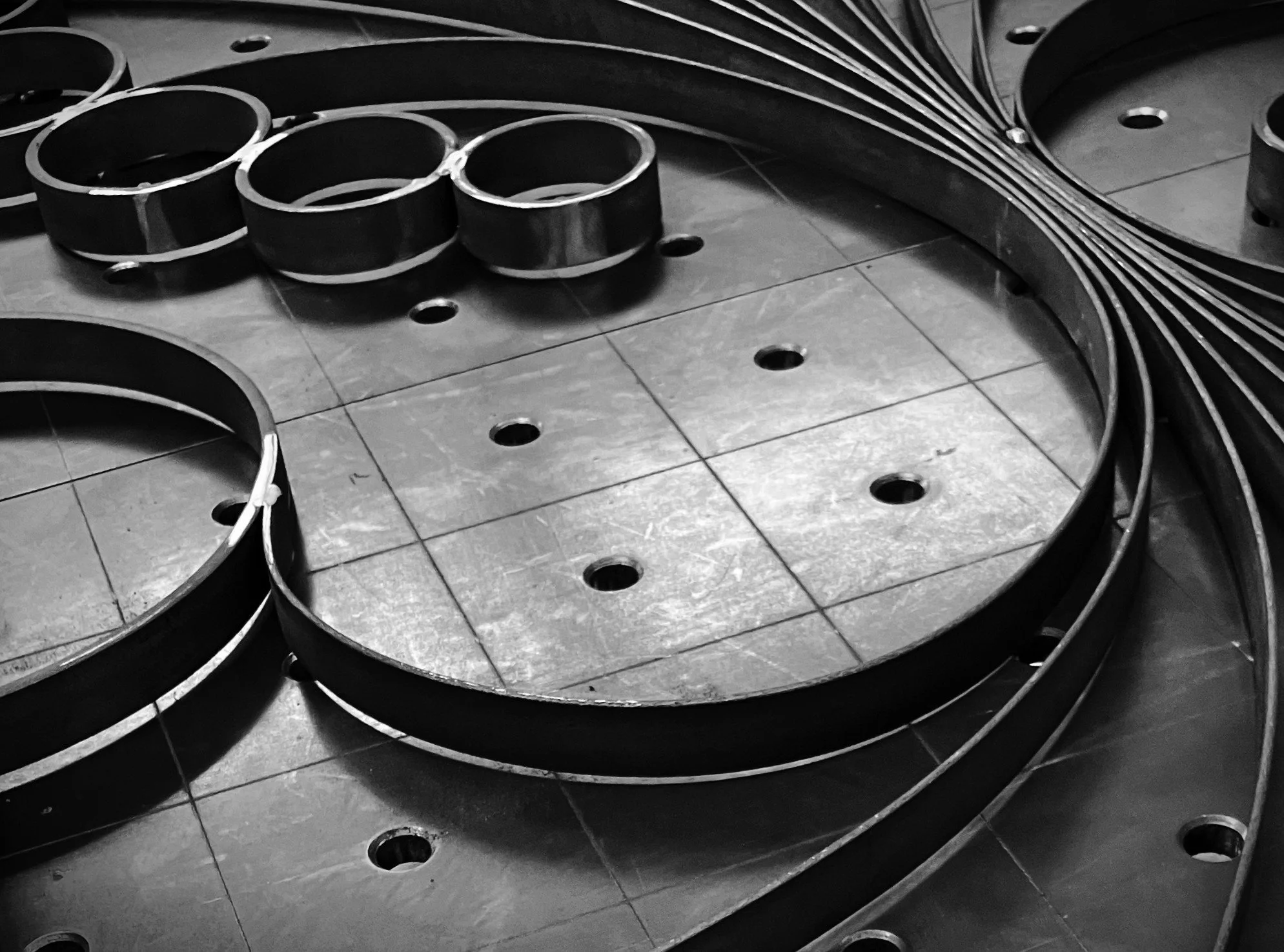Stacks of large black circular metal scrolls on a work table in an industrial setting.