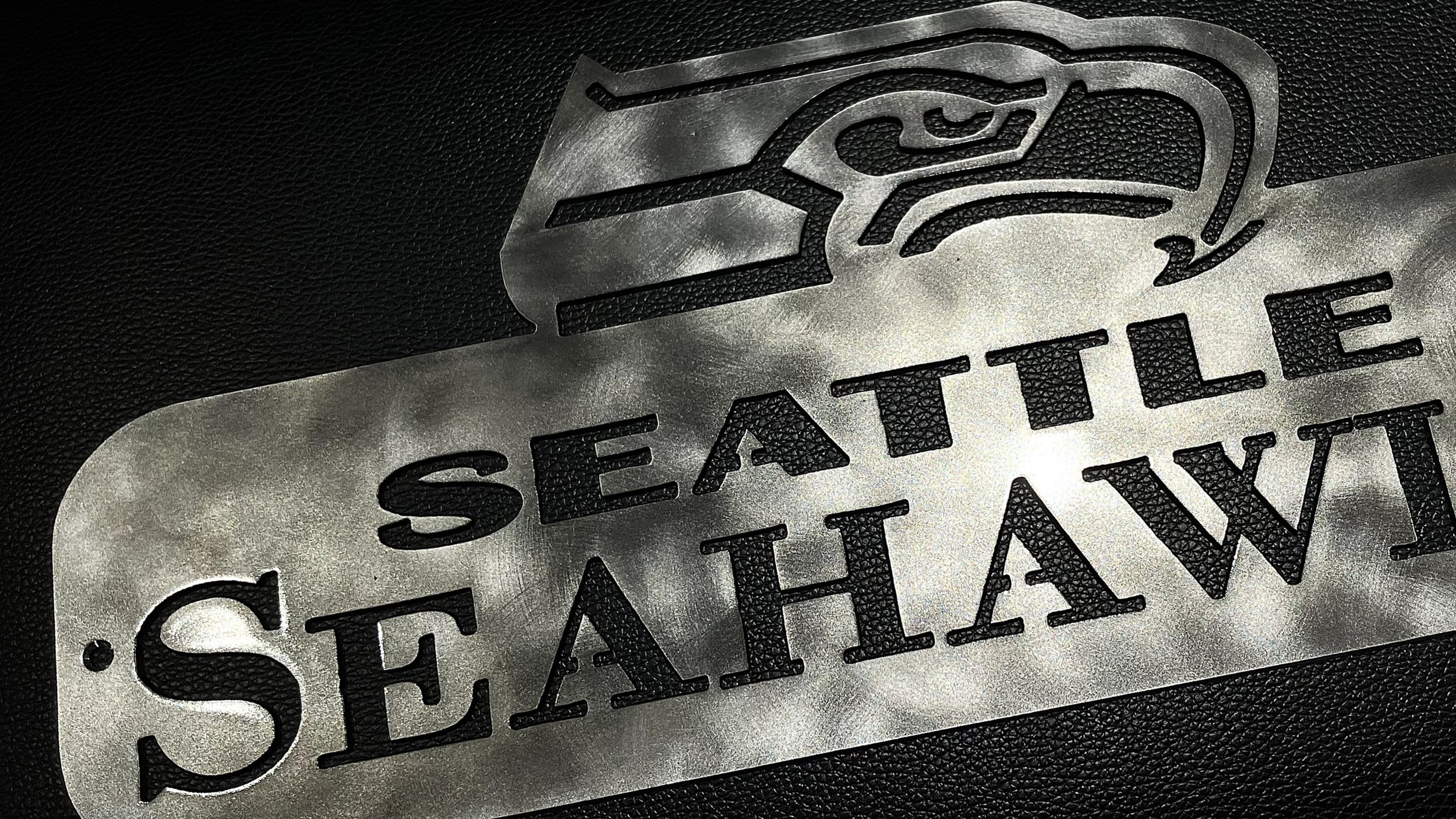 Close-up of a metal artwork with the Seattle Seahawks logo and text on a black textured background.