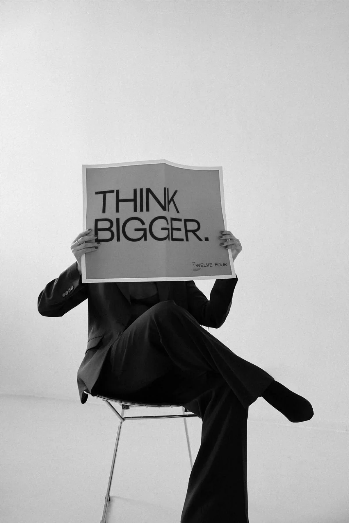 Schwarzer und weißer Stuhl mit Person in Schwarz sitzt und hält ein Schild mit der Aufschrift "THINK BIGGER."