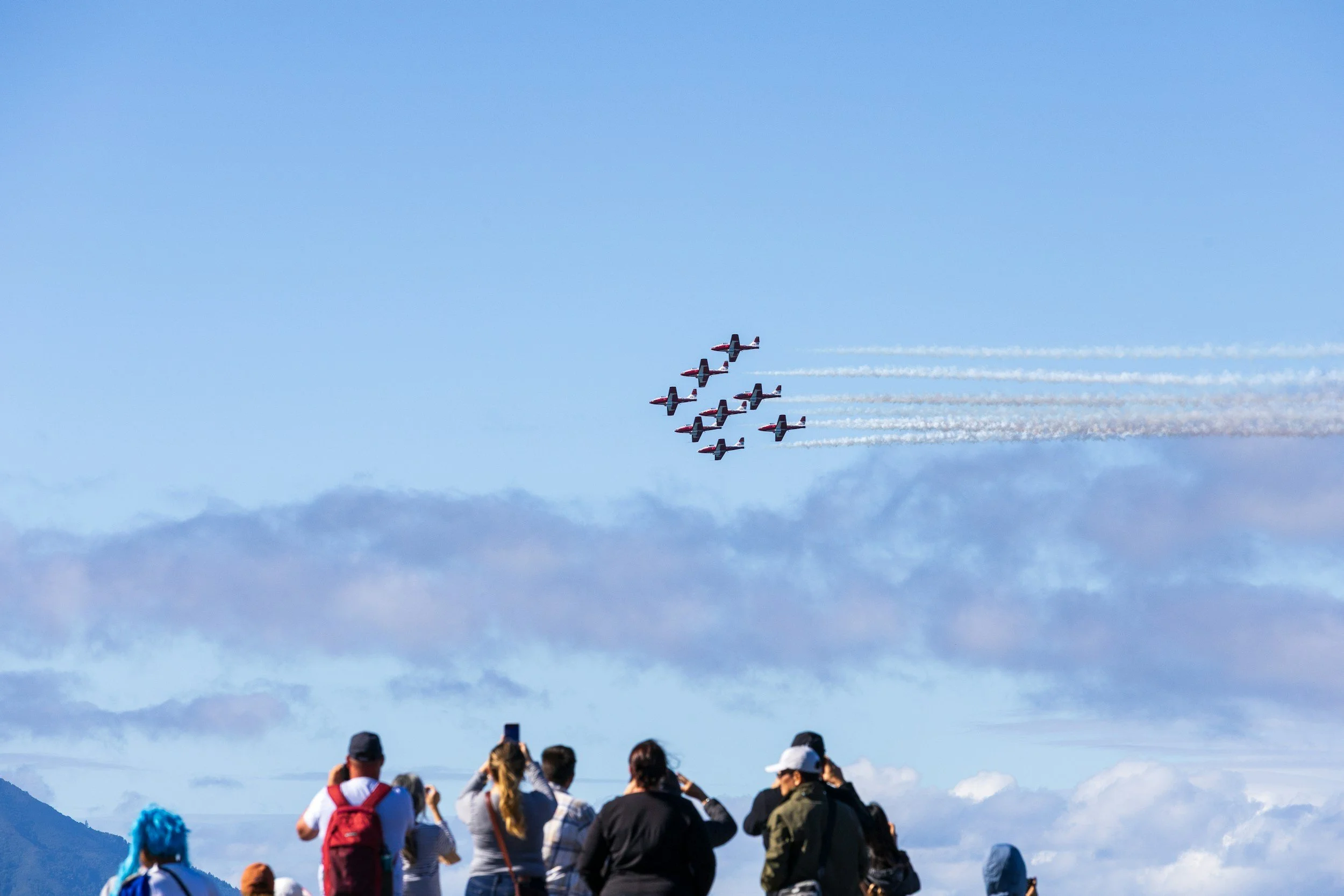 Group of spectators watching an airplane flying in formation in the sky at an airshow.