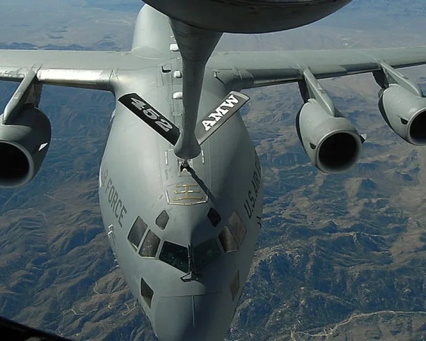 A military cargo aircraft flying over a landscape, viewed from above, with visible engines and the U.S. Air Force markings.