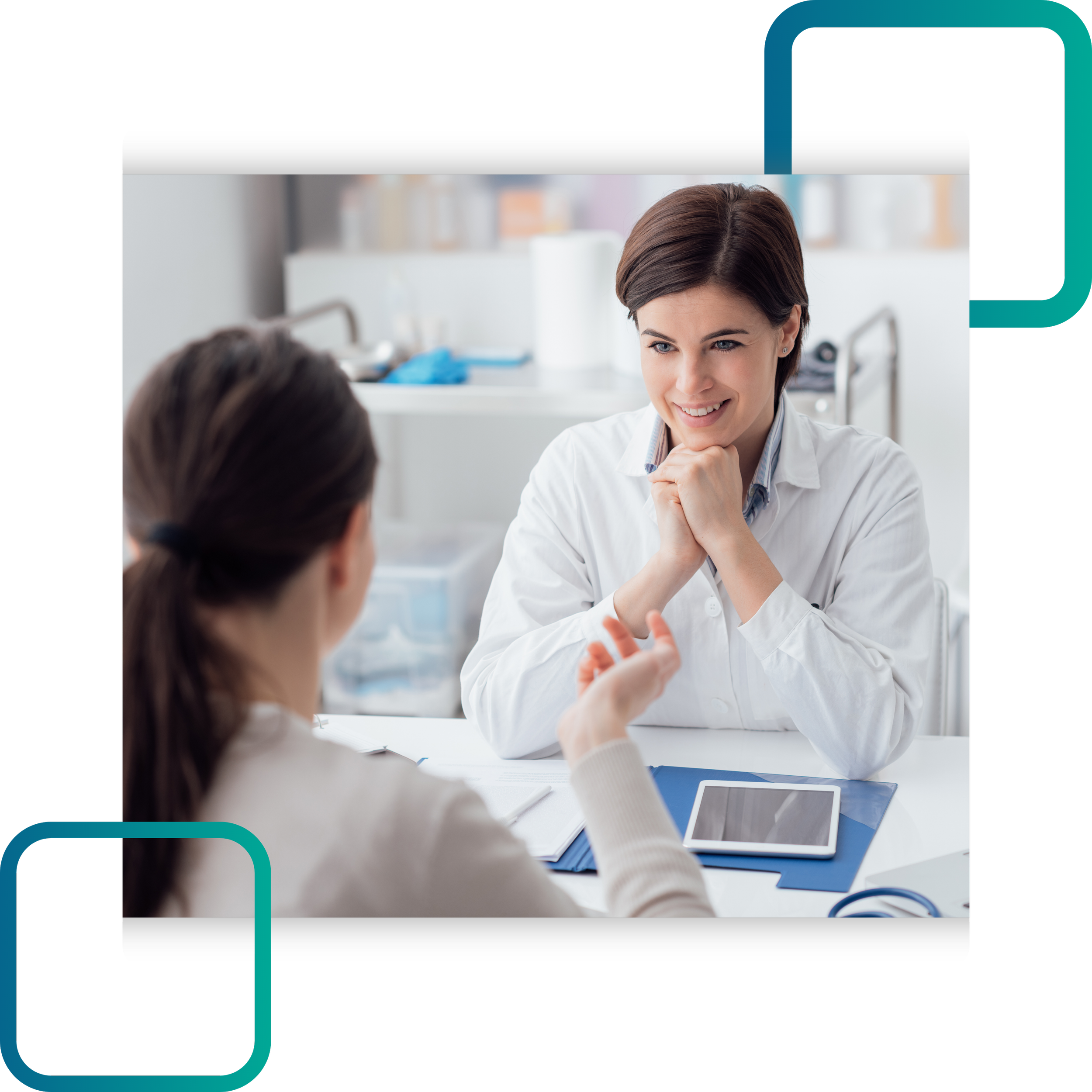 A smiling female healthcare worker in a white coat sitting at a table in a clinical setting, engaging in conversation with a patient. The table has a tablet device, papers, and medical supplies.