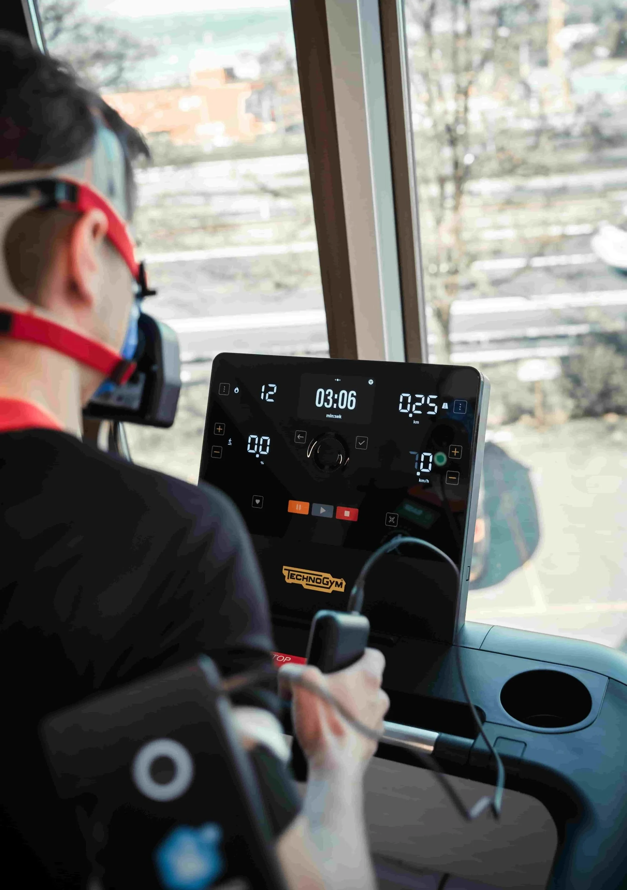 Person auf einem Laufband in einem Bus trägt einen Schutzhelm und benutzt ein Herzfrequenzmessgerät, während die Anzeige die Laufzeit und Geschwindigkeit zeigt.