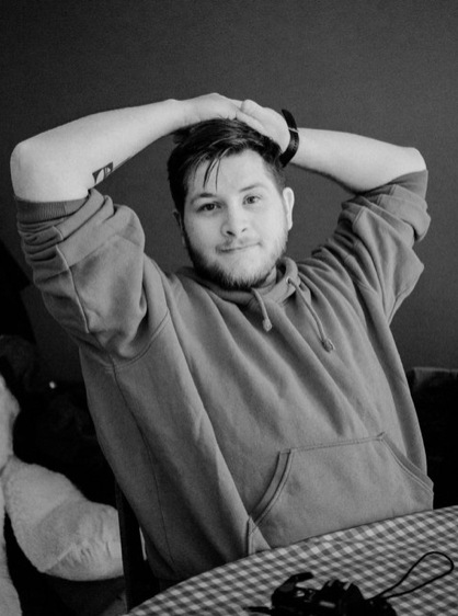 Black and white photo of a person in a hoodie sitting at a checkered table.
