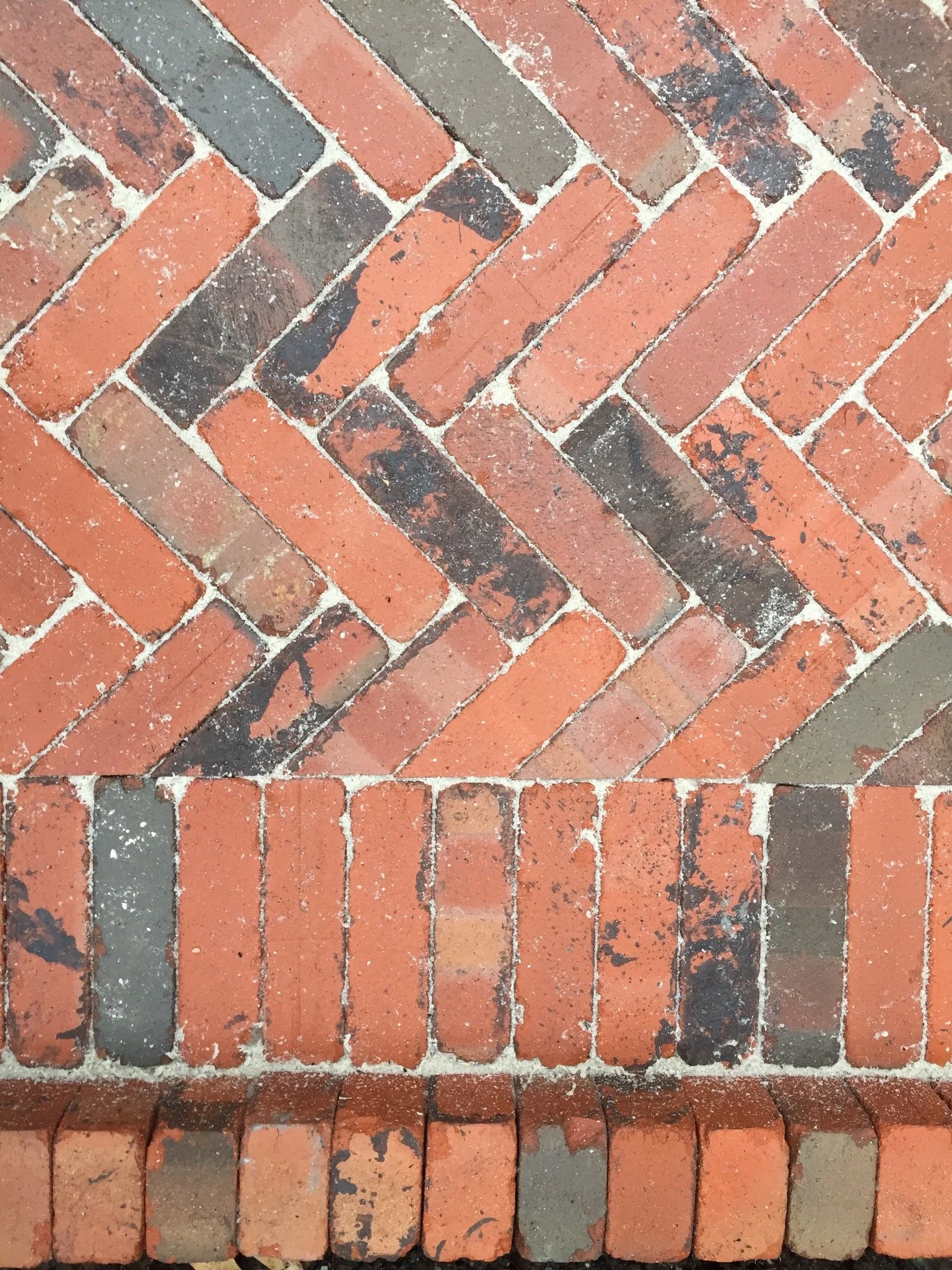 Close-up of a brick sidewalk arranged in a herringbone pattern with some bricks showing black soot and wear.