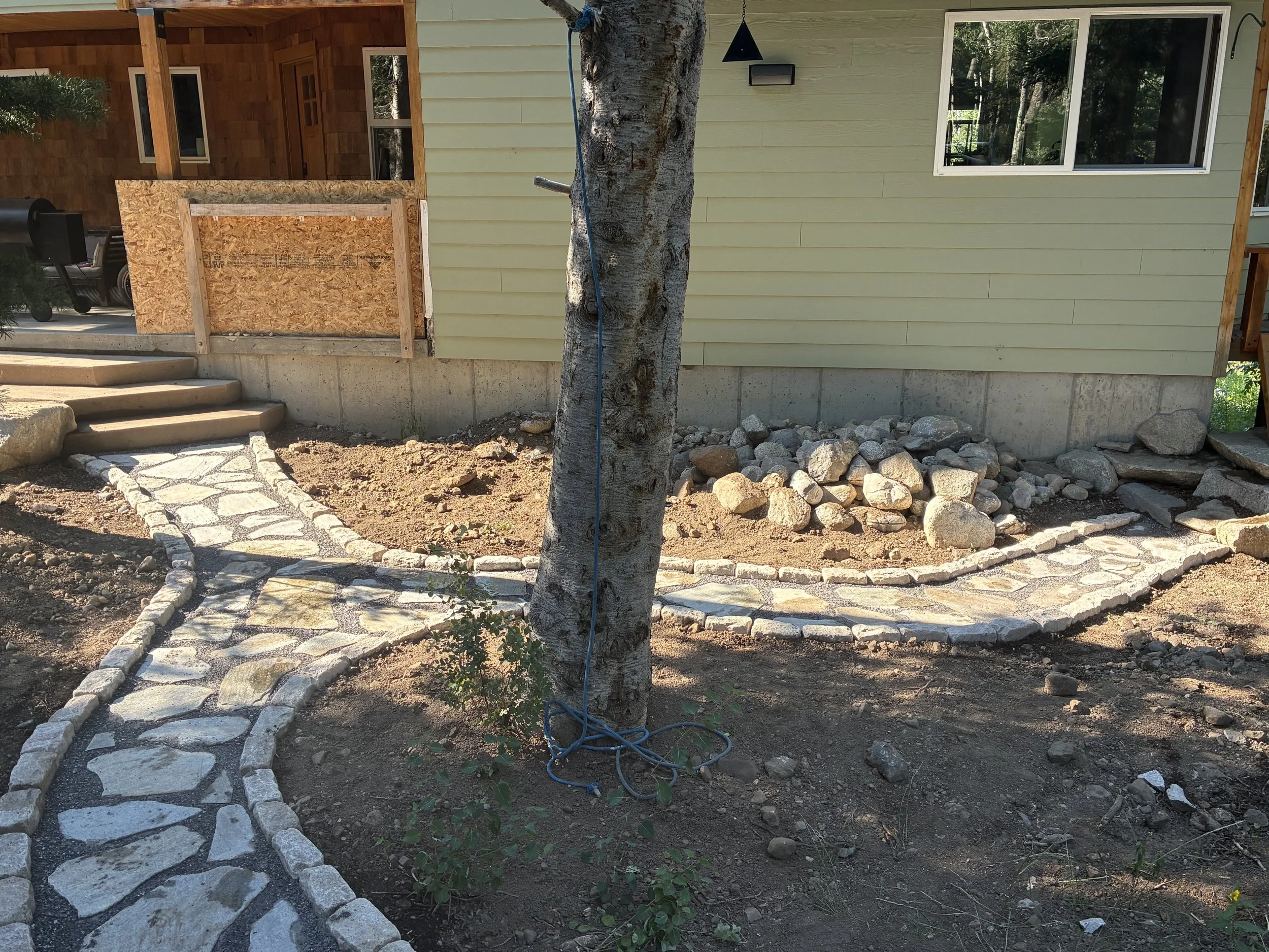 A backyard garden with a stone pathway, concrete steps, good hardscaping, and a tree.