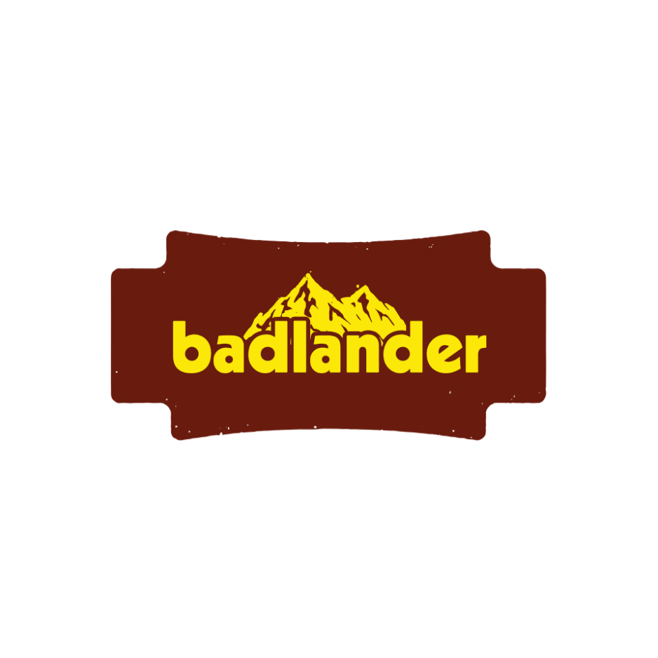 Badlander Beverages: A vintage badge logo for Badlander Beverages with bold yellow lettering on a deep brown distressed emblem and a mountain range illustration, reflecting Montana's rugged craft spirit.