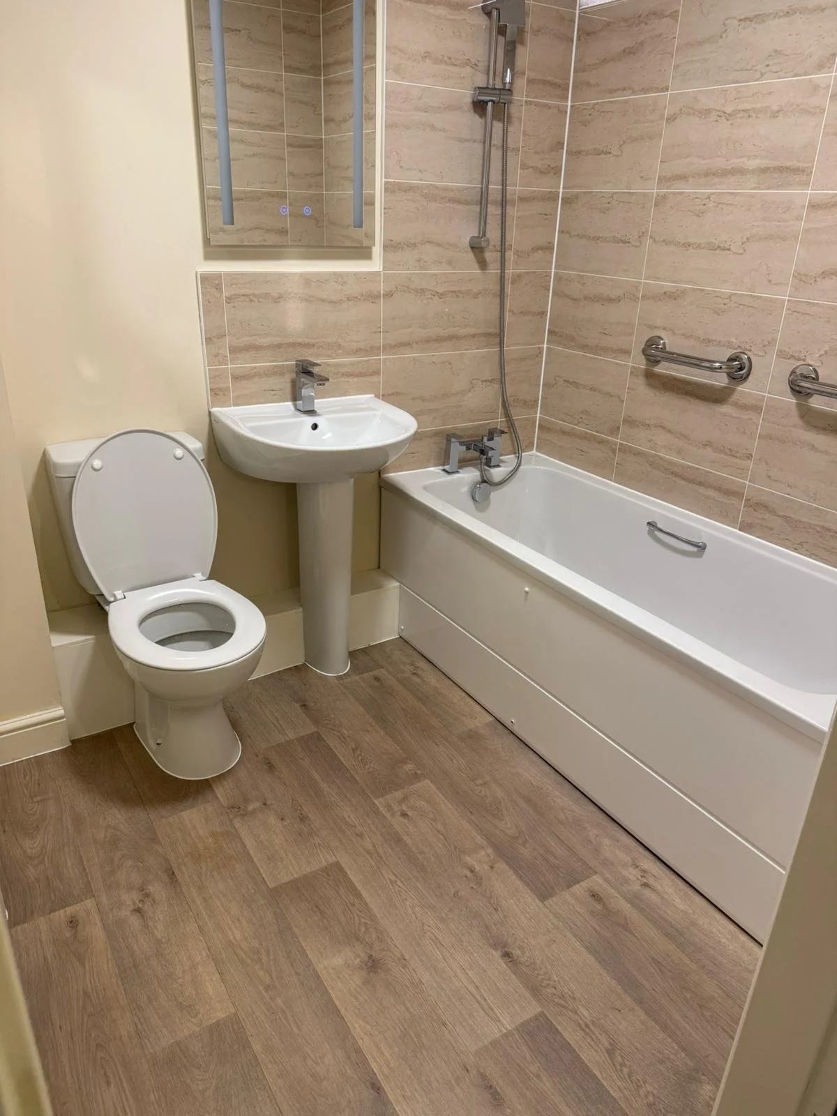 Bathroom with toilet, pedestal sink, bathtub with shower, and grab bars on the wall.