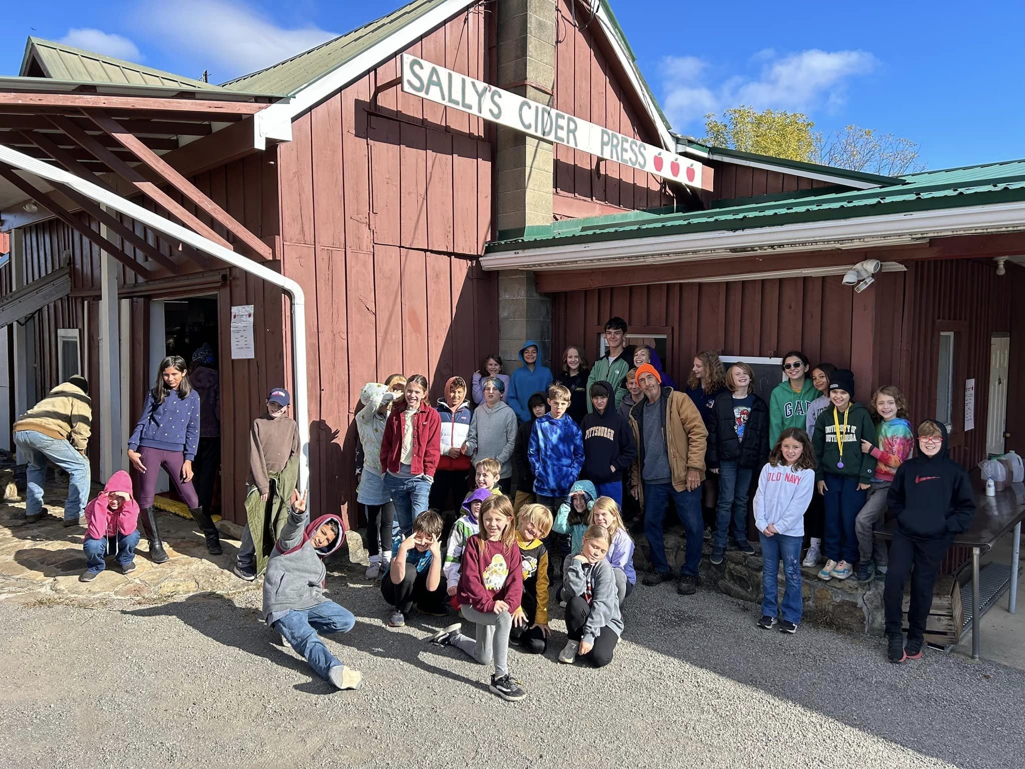 Elementary students from explore an apple orchard during a field study day, walking among apple trees and observing nature outdoors.