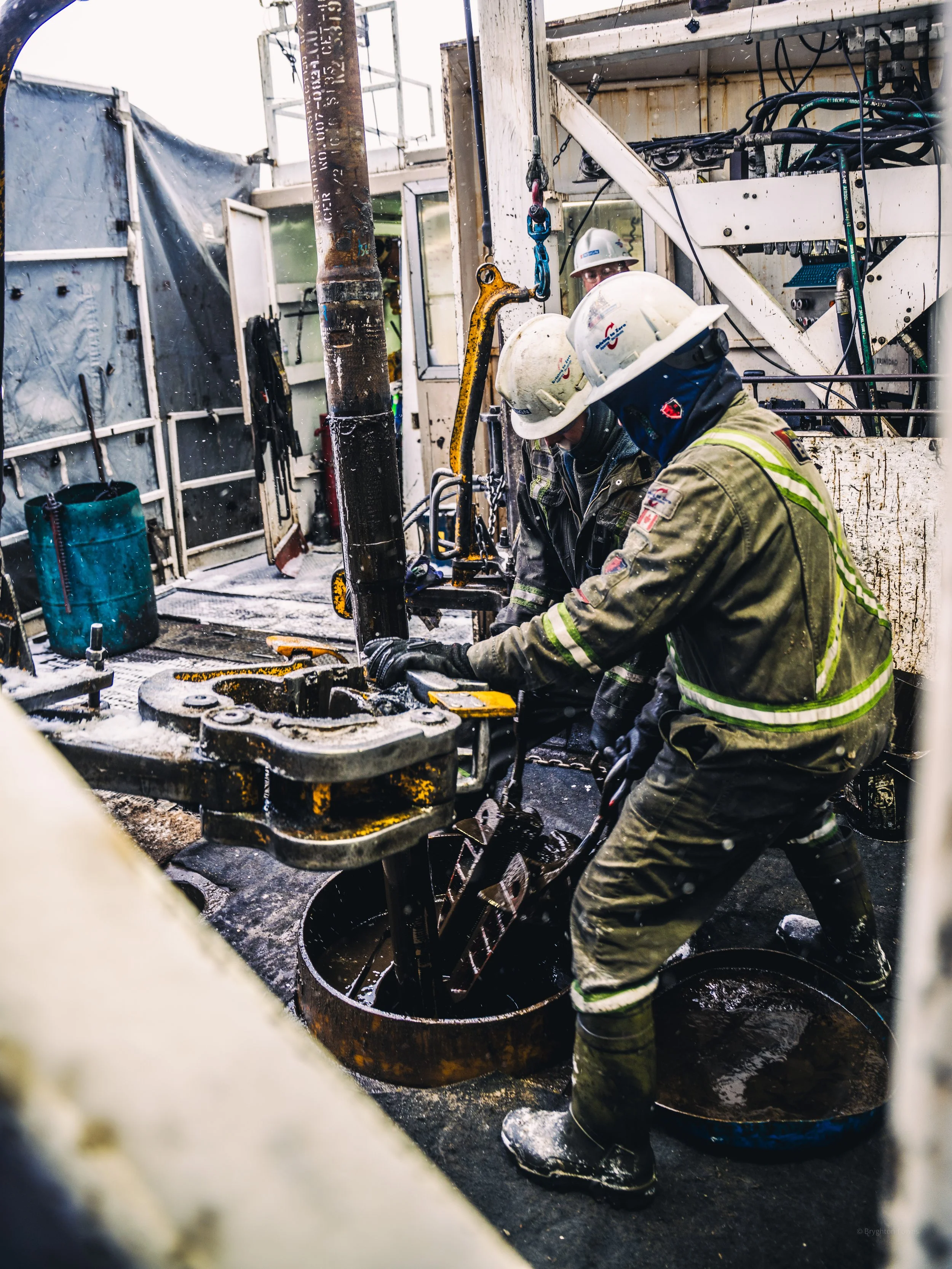 Workers in protective gear operating heavy machinery on an offshore oil rig, with pipes, equipment, and safety gear.