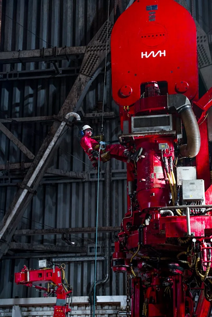 A worker in safety gear is climbing and performing maintenance on a large red industrial machine inside a metal structure.