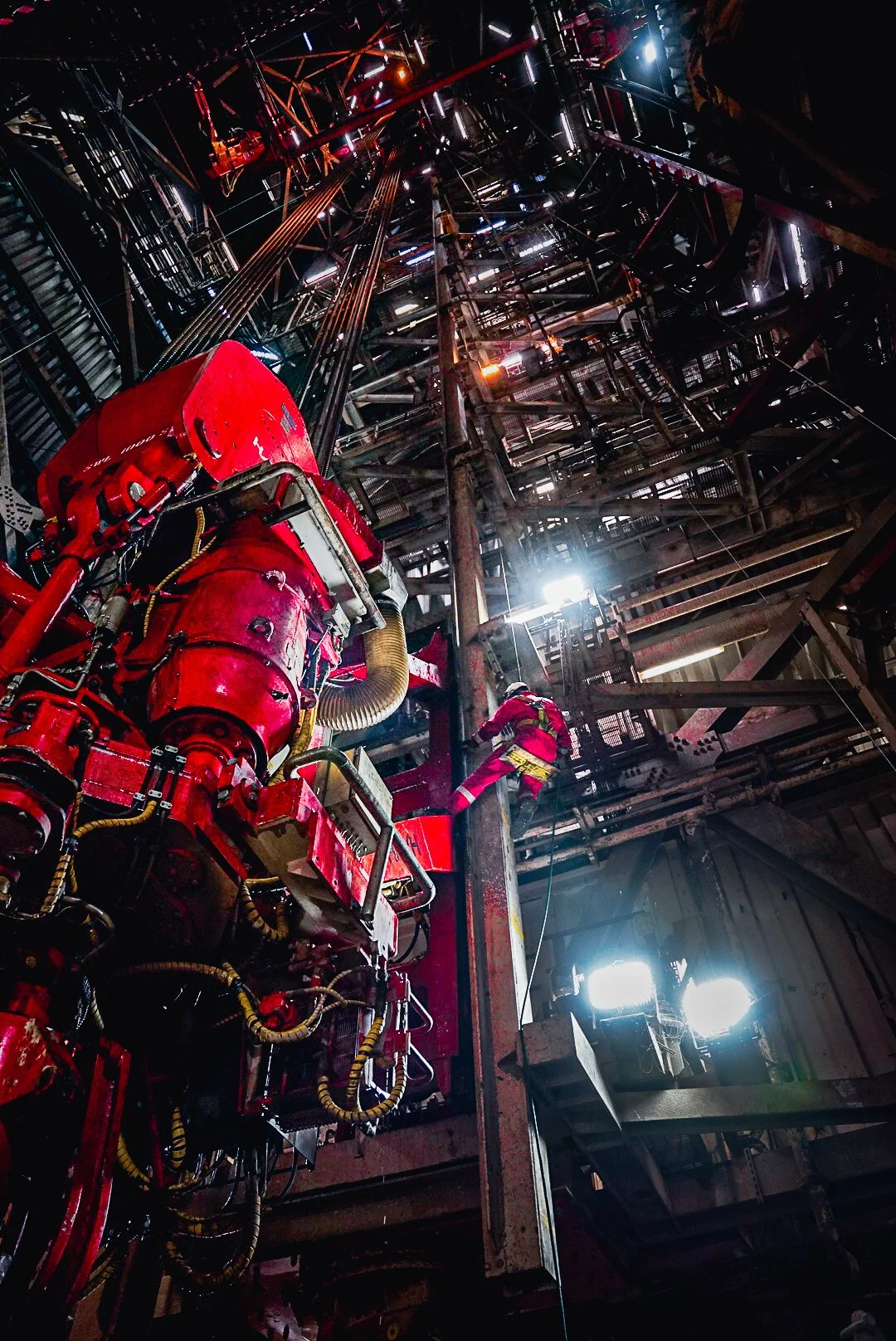 A worker in red safety gear climbing inside an industrial facility with complex machinery and metal scaffolding, illuminated by bright lights.