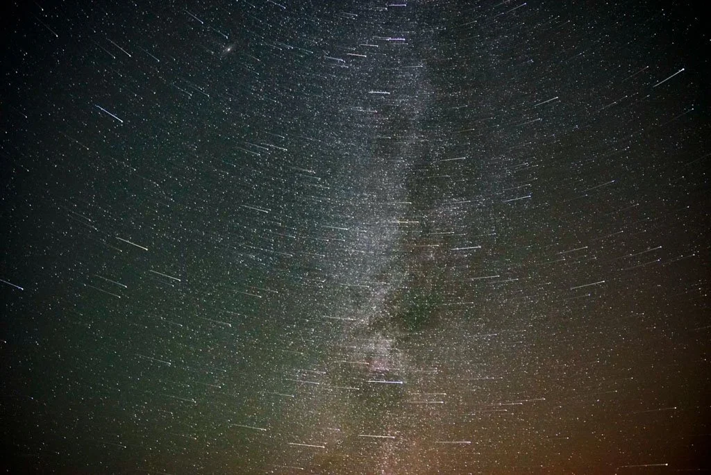 Night sky filled with stars and the Milky Way, with star trails indicating long exposure.