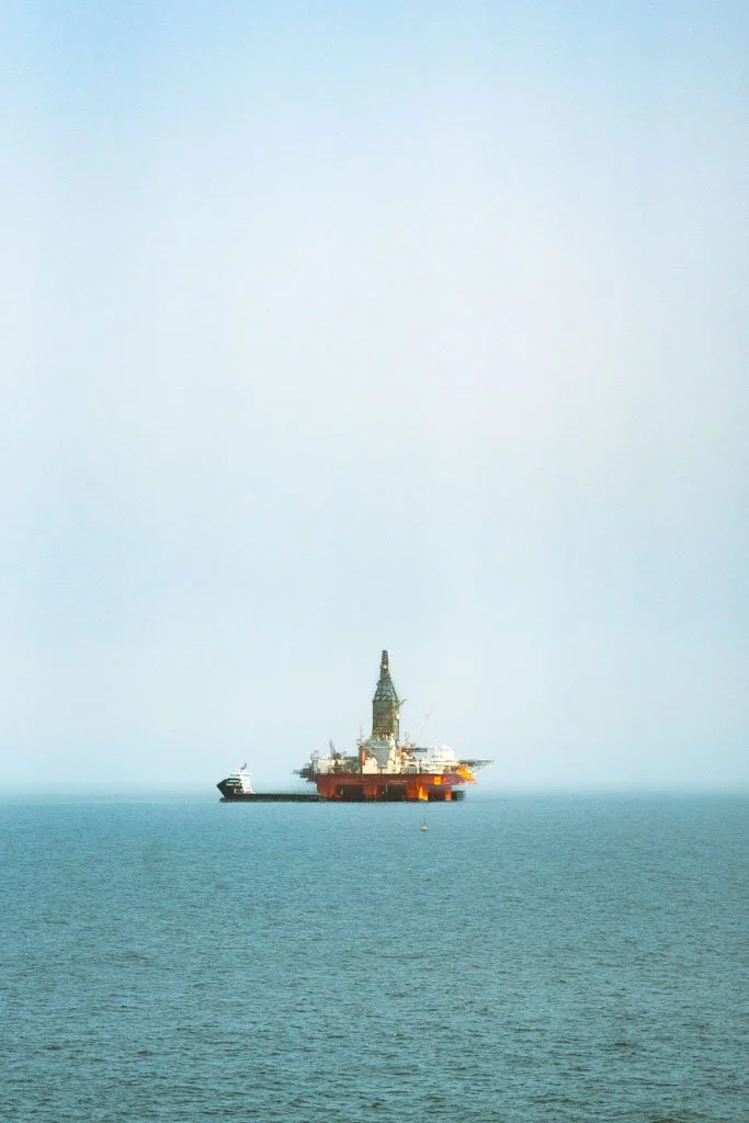 Offshore oil rig in the ocean with a ship nearby under a clear sky.