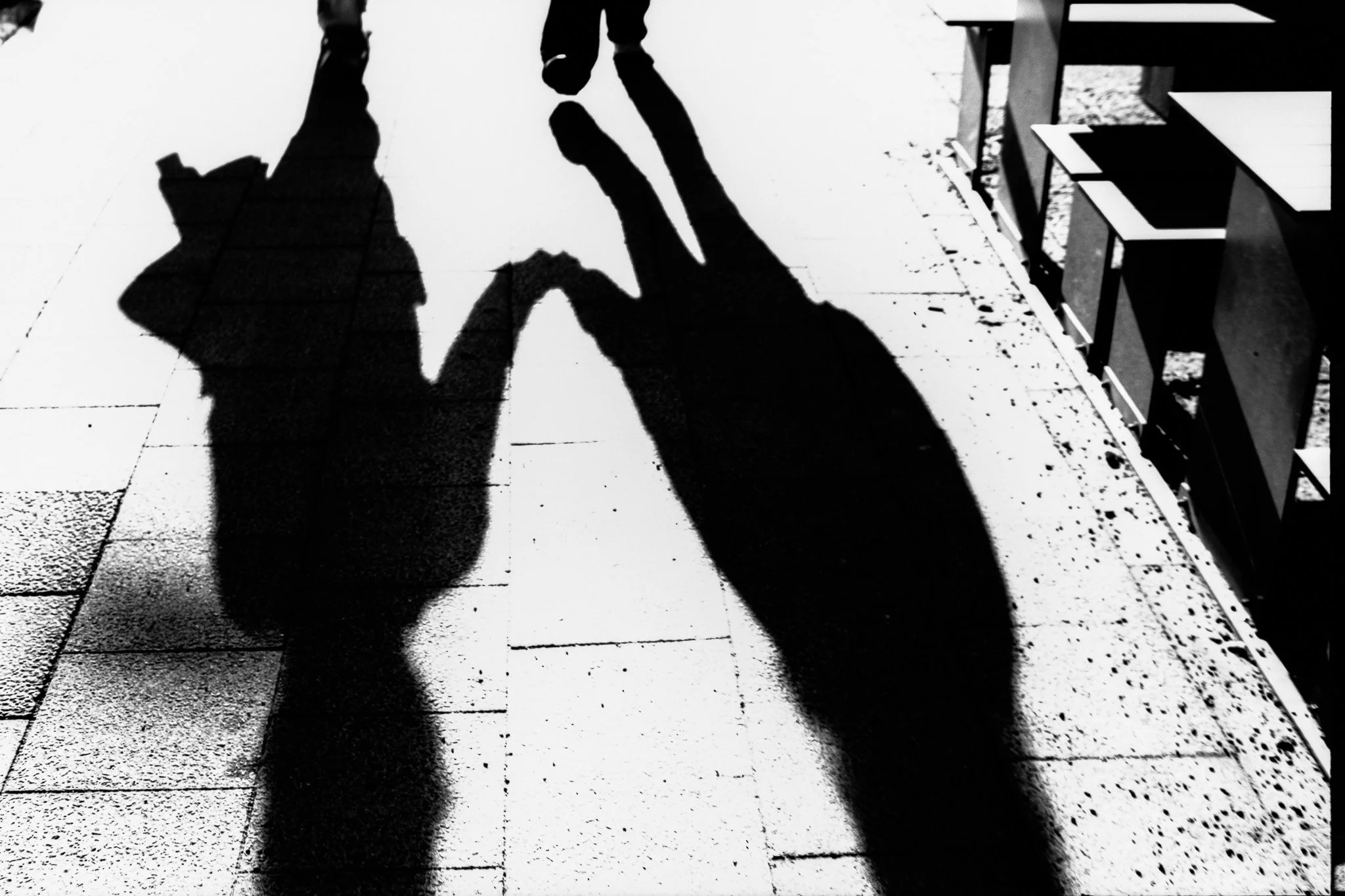 Silhouettes of two people holding hands, casting shadows on the sidewalk.
