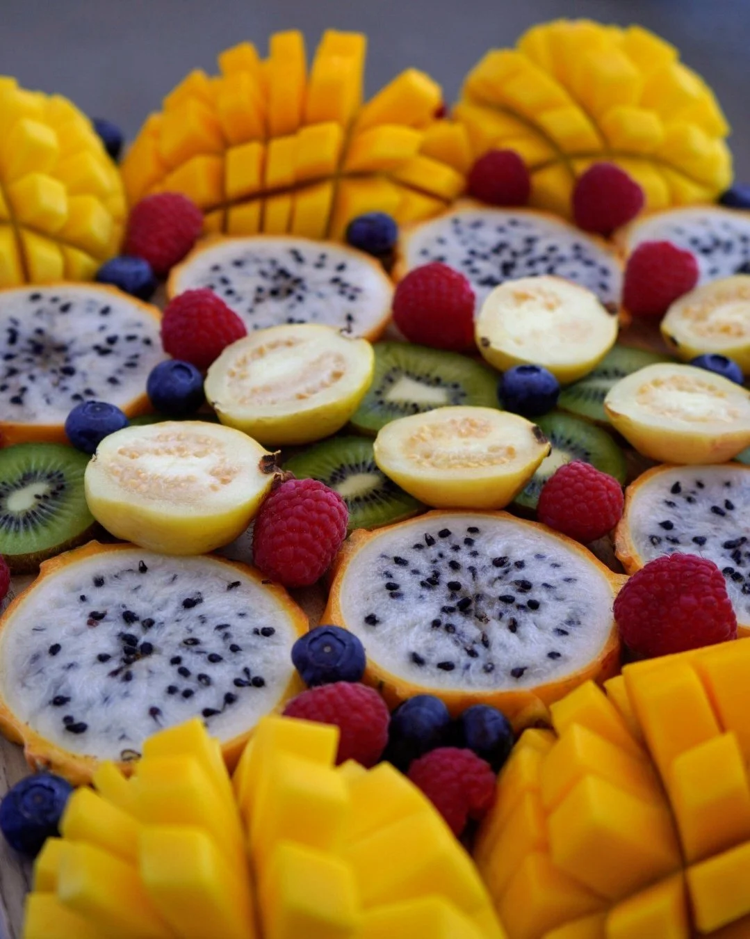Close up of a tropical raw vegan fruit platter made with mangoes, yellow pitaya, raspberries, blueberries, guava, and kiwis.