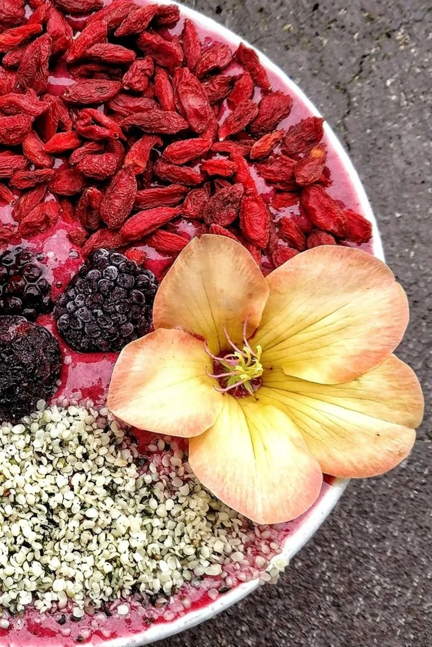 Strawberry banana raw vegan smoothie bowl topped with hemp seeds, goji berries, and a plumeria flower.
