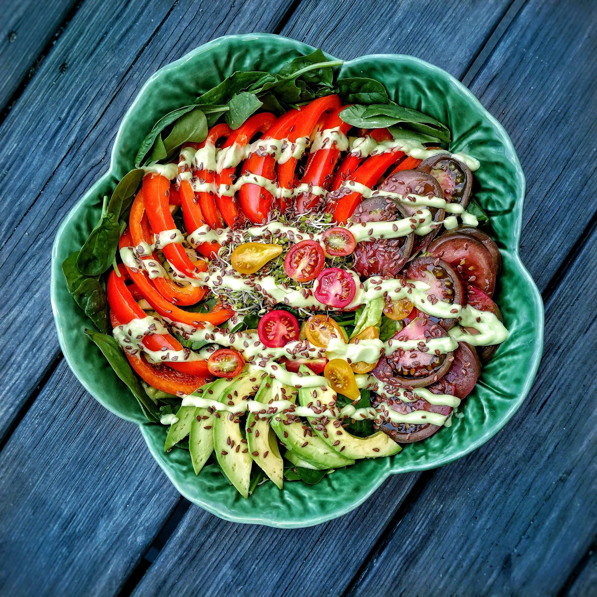 Very nicely arranged raw vegan salad composed of red bell pepper, heirloom cherry tomatoes, kale, and sliced avocado. Topped with flaxseed and dressed with a raw vegan avocado lime dressing.