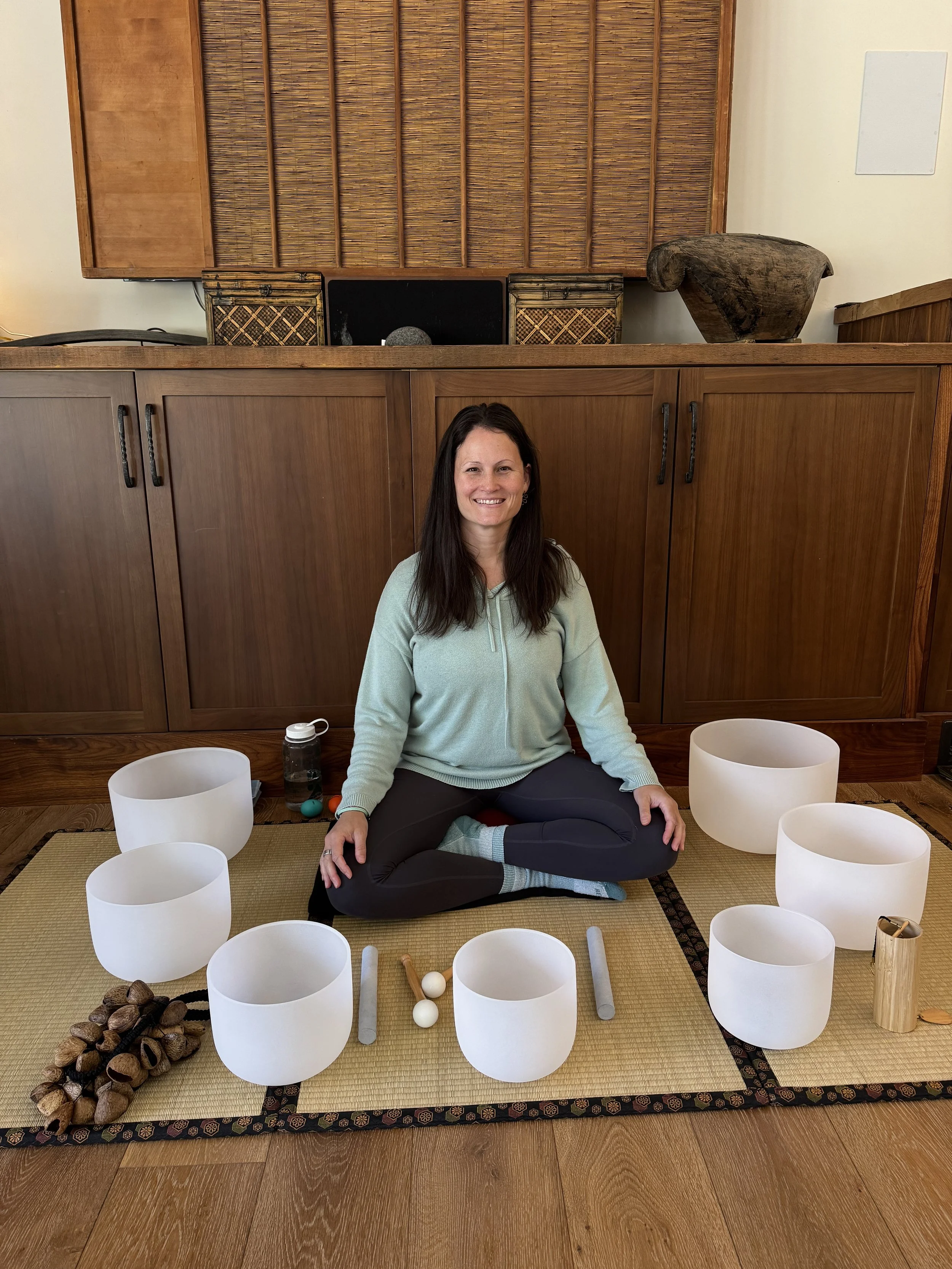 A woman sitting in front of crystal singing bowls sitting atop a tatami mat.