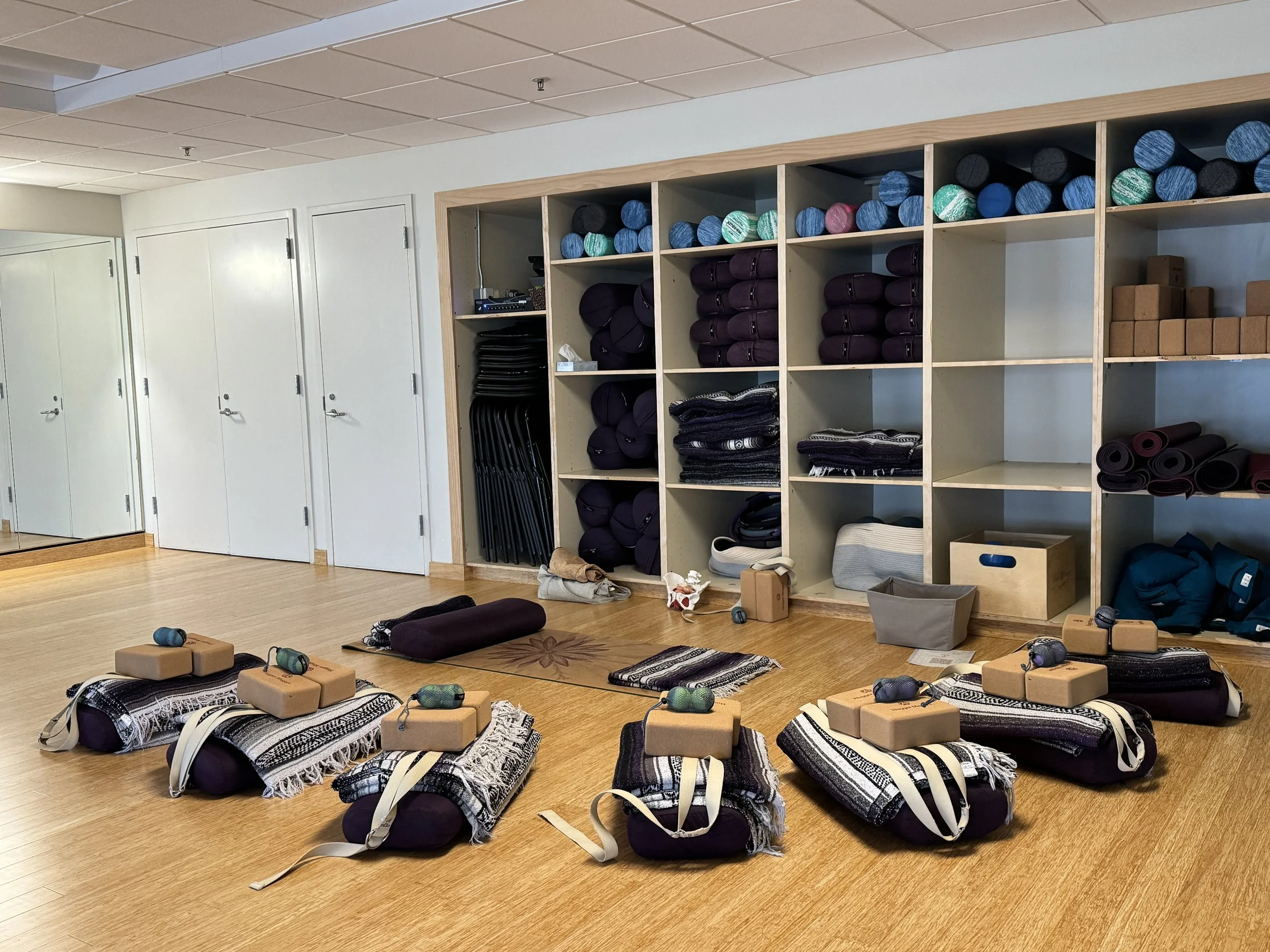 A yoga studio set up with props next to a wall with more props in preparation for a class.