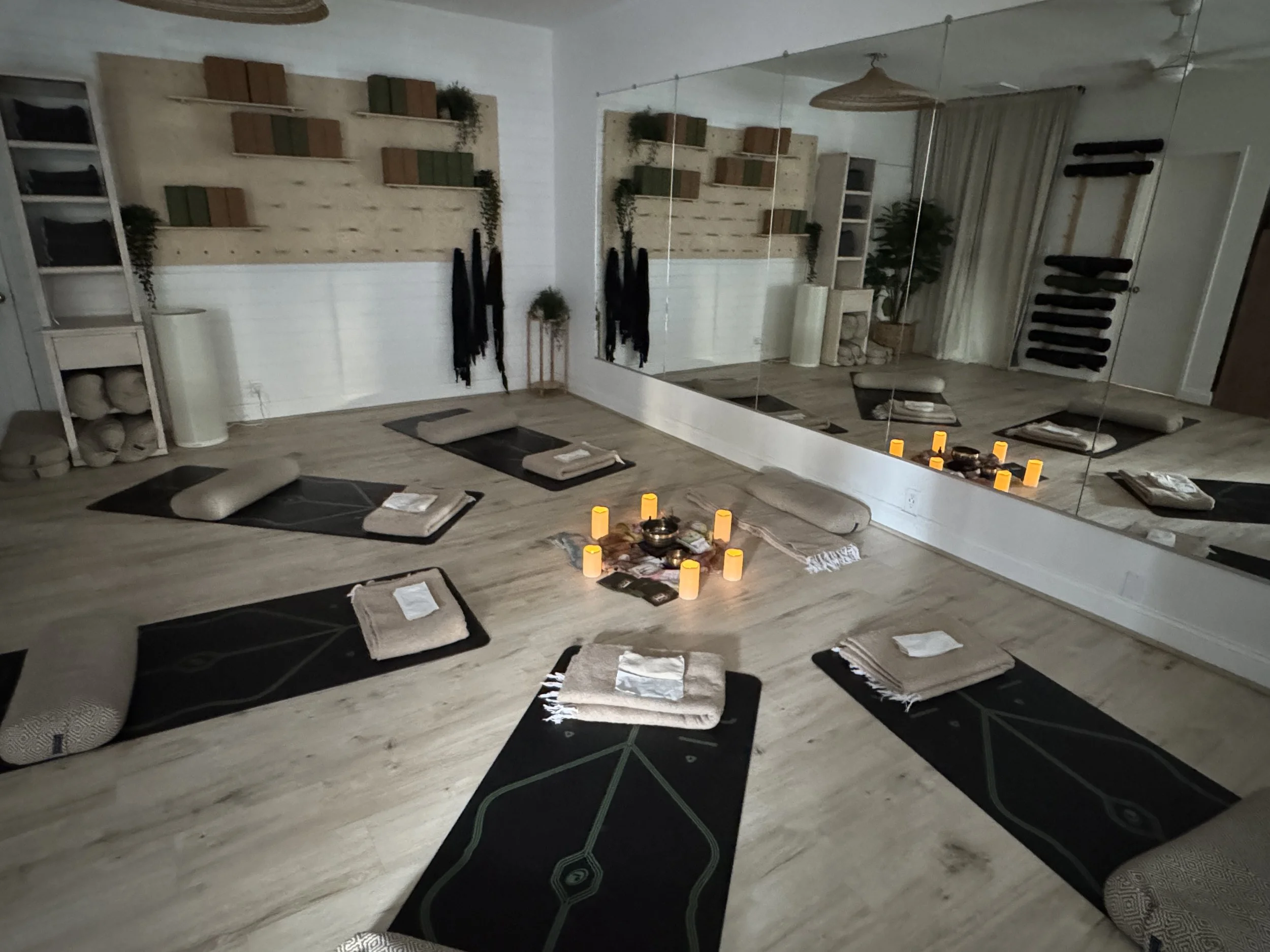 A room with a large mirror on one wall, and props on the other wall with mats set up for a reiki and meditation session and an altar with candles in the middle.