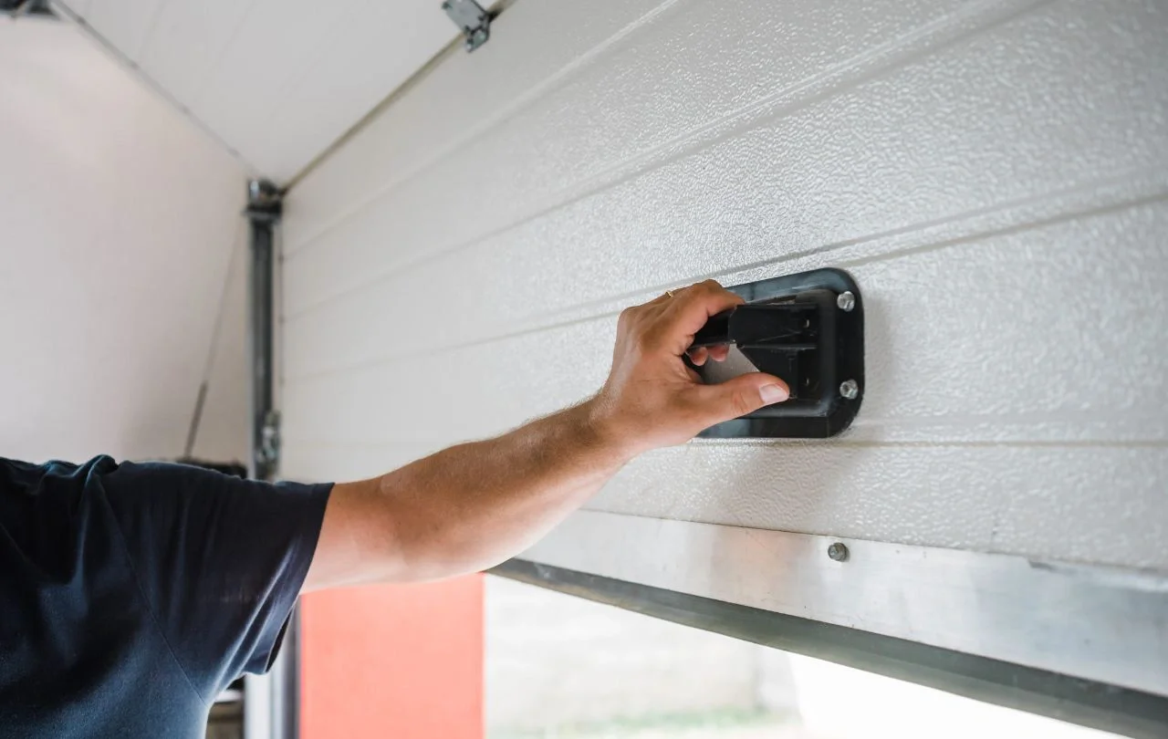 A person pulling down a garage door lock latch on a white garage door.