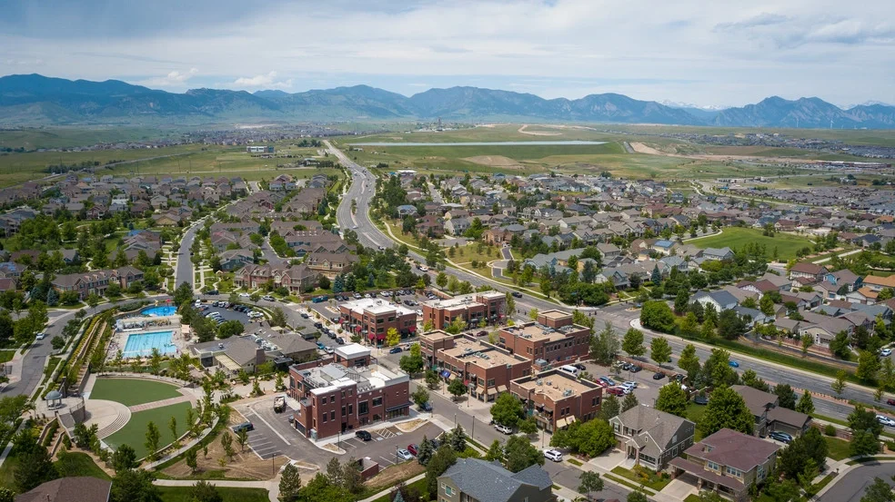 Aerial view of a suburban neighborhood with residential houses, a community pool, and mountains in the background.