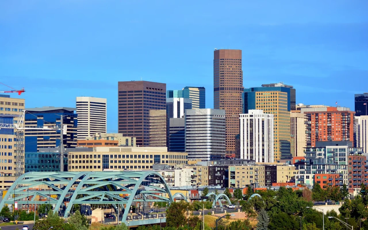 A city skyline with tall buildings, some of which are under construction, and a bridge in the foreground on a clear day.