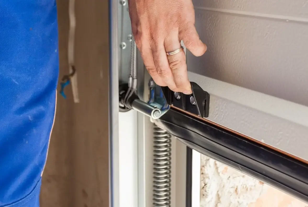 A person installing or repairing a garage door with hand on metal track and garage door opener mechanism.