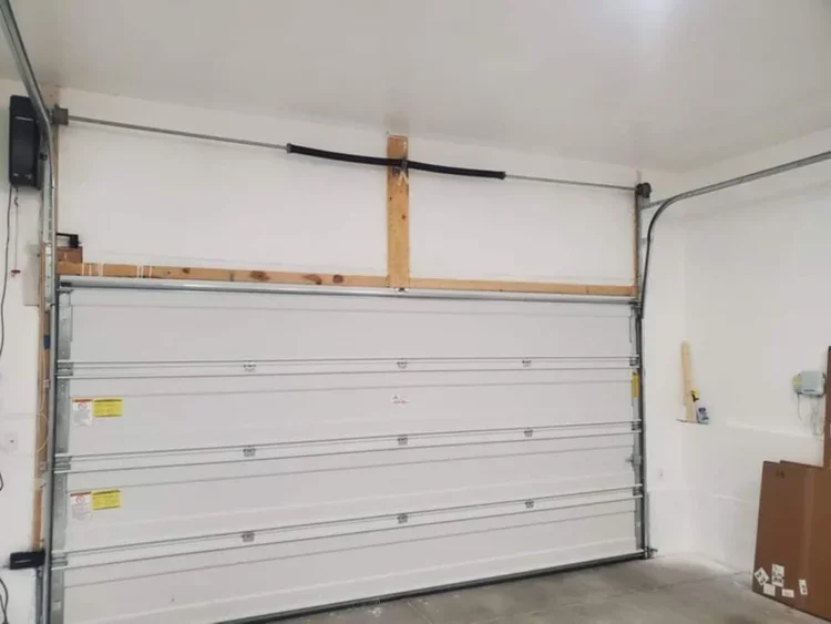 Empty white garage door in a garage with unfinished wall and some tools and boxes nearby.