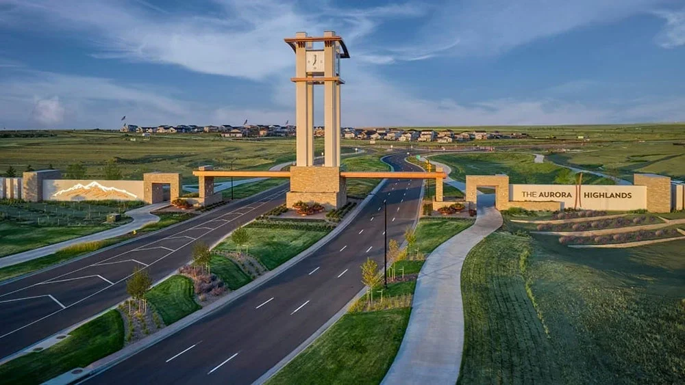 Entrance gate to The Aurora Highlands community with a tower, signage, and landscaped surroundings, under a blue sky.