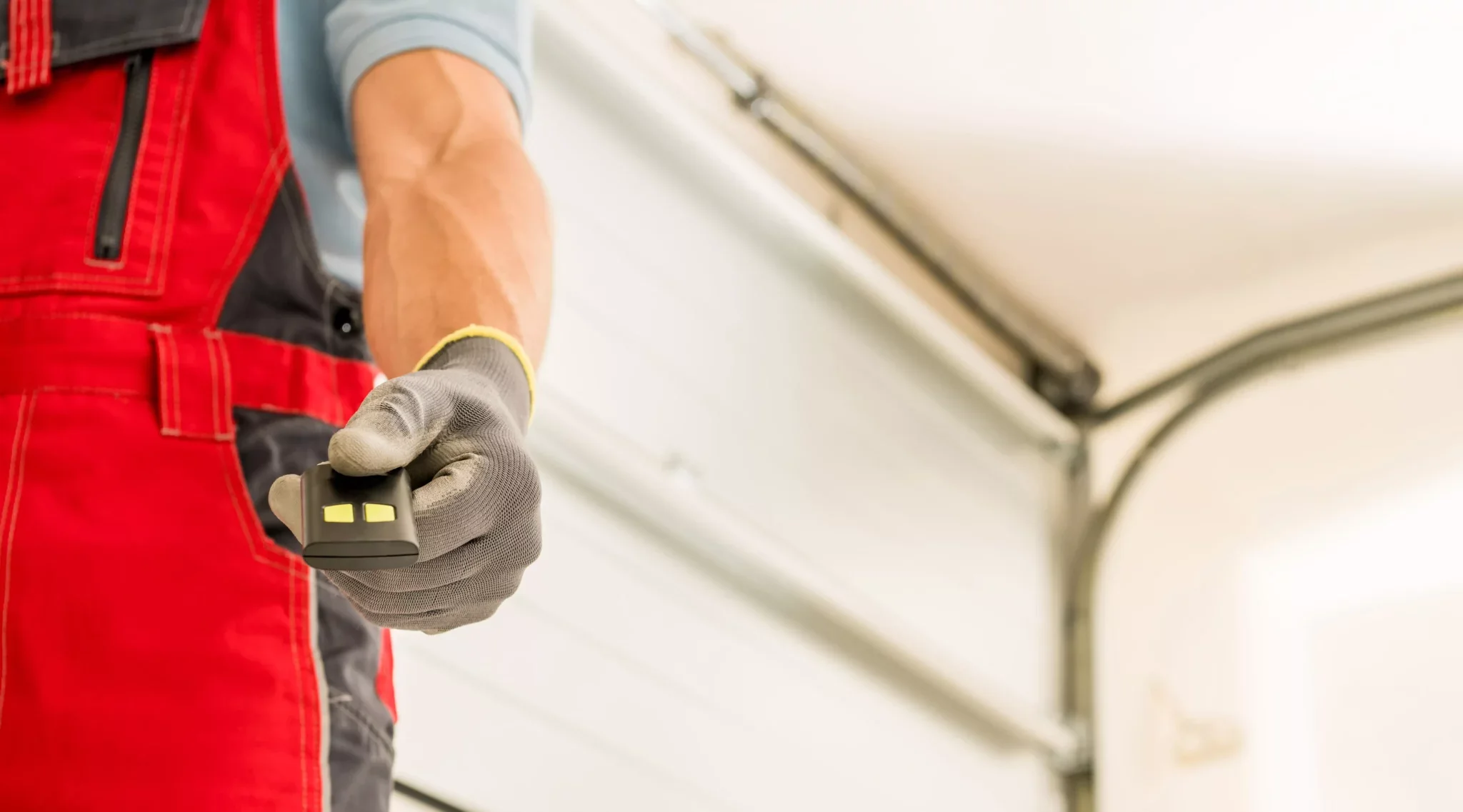 Person wearing gray gloves holding a remote control in a garage with a white door and metal ceiling.