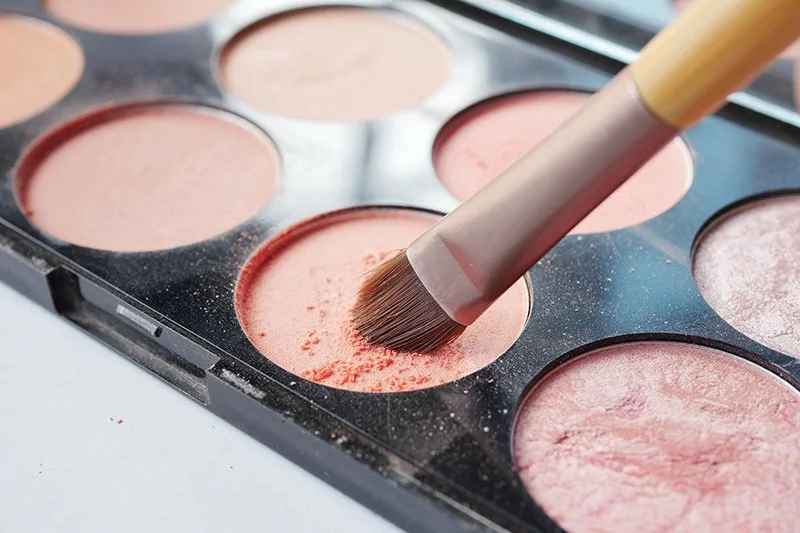 Close-up of a makeup palette with pink blush and a makeup brush.