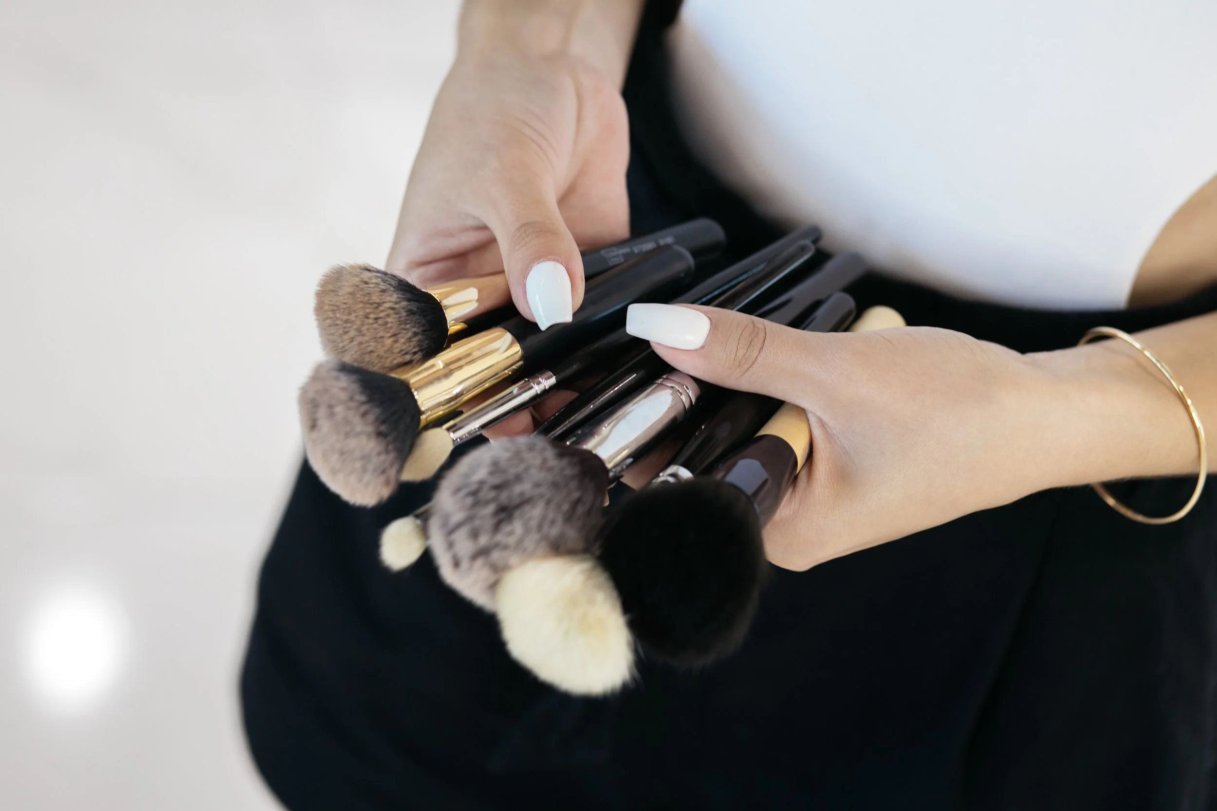 A professional makeup artist holds a collection of makeup brushes with white painted nails.