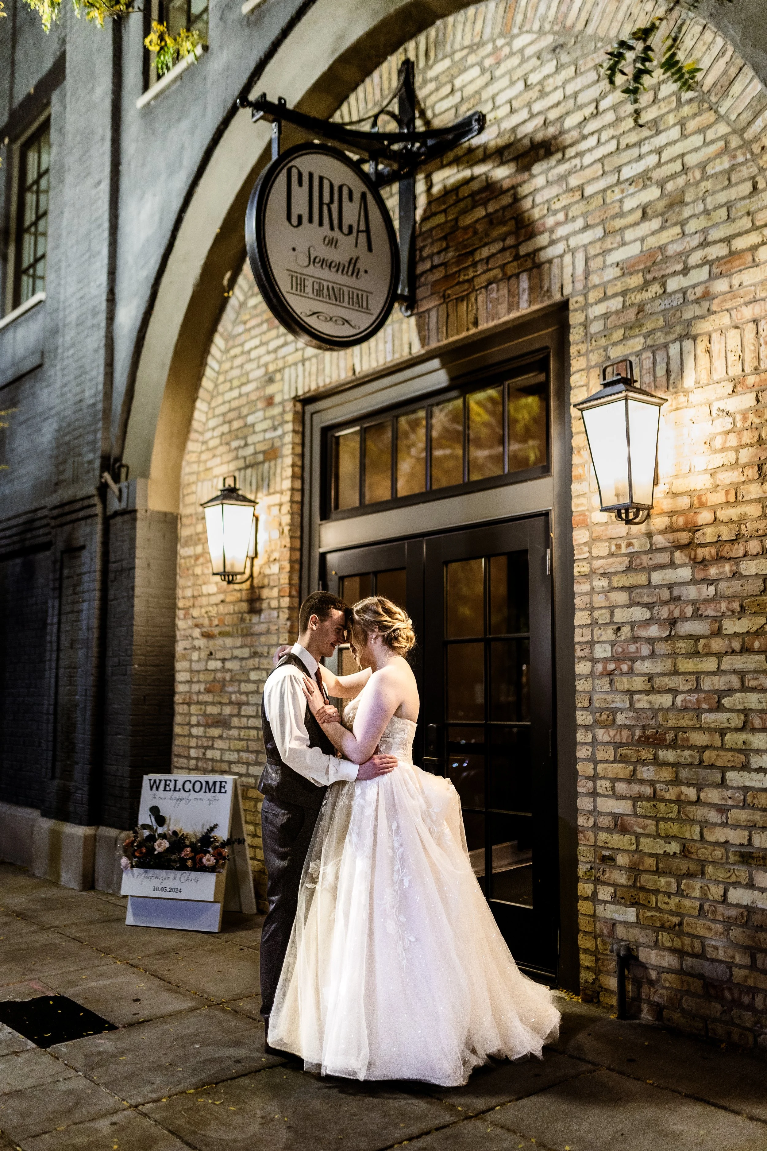 A bride and groom sharing a moment outside Circa on Seventh in Kenosha, WI. The couple is dressed in wedding attire, standing close with foreheads touching and eyes closed, holding each other.