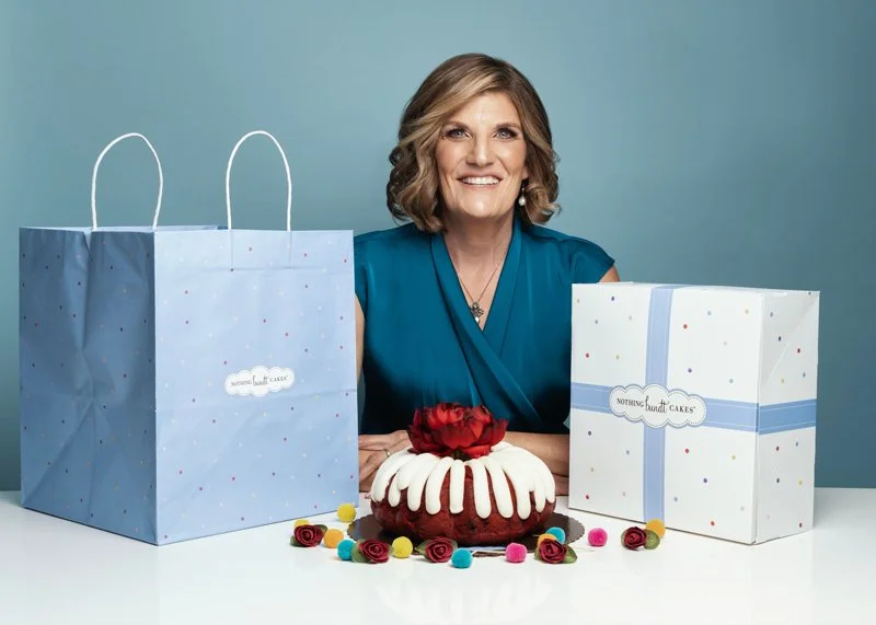 A smiling business woman with professionally applied makeup in a teal dress poses for branding photos for her bakery business.