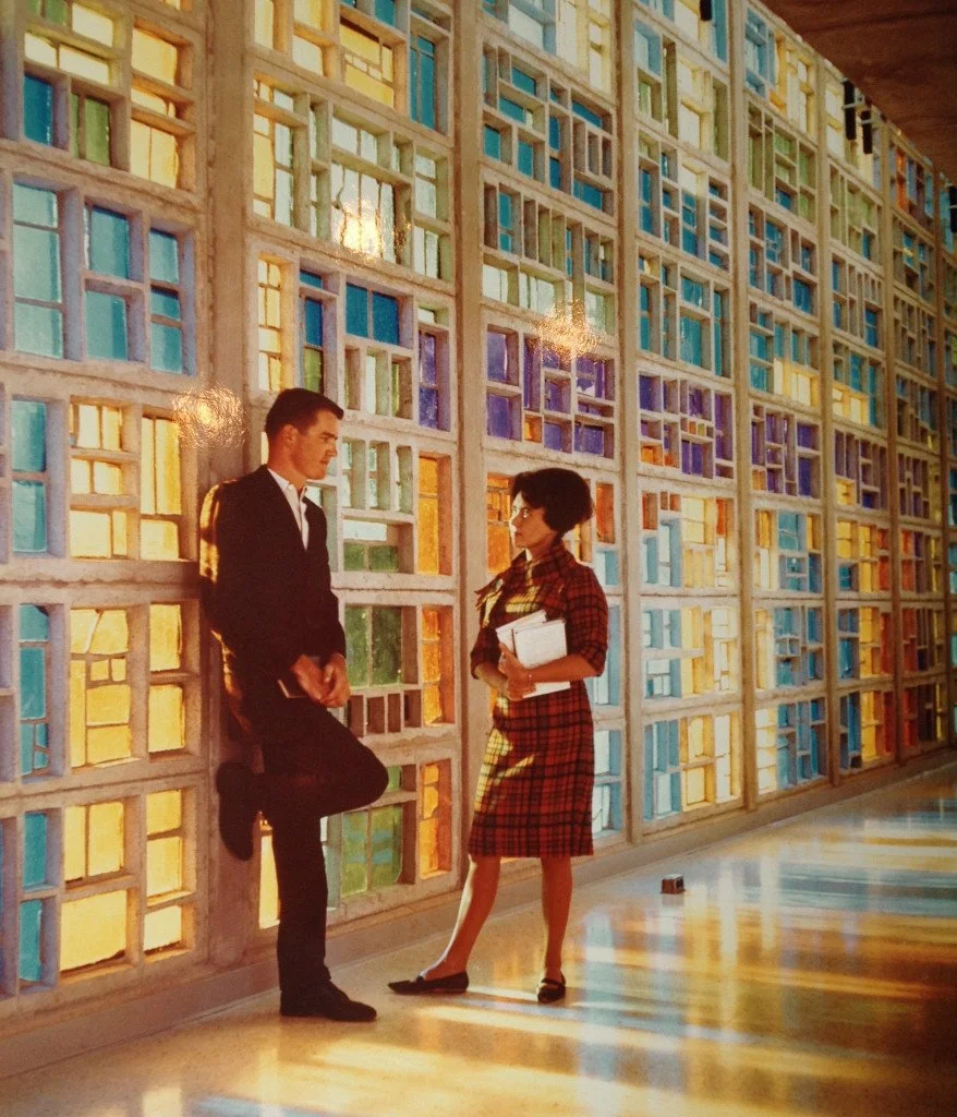 A man and woman talking in front of a colorful stained glass wall.