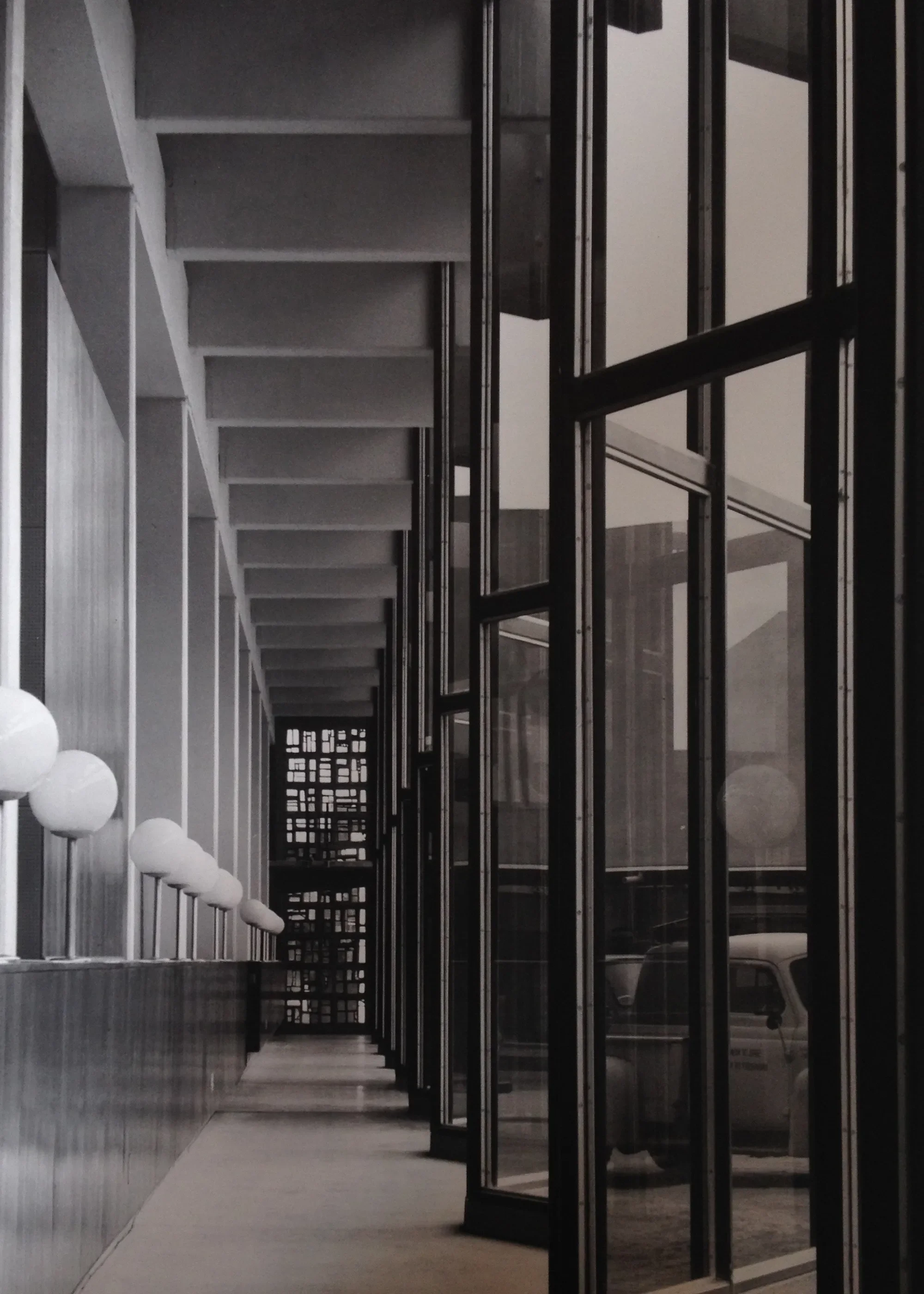 Modern building entrance with glass doors, white spherical light fixtures on the left, and a corridor with stairs in the background.