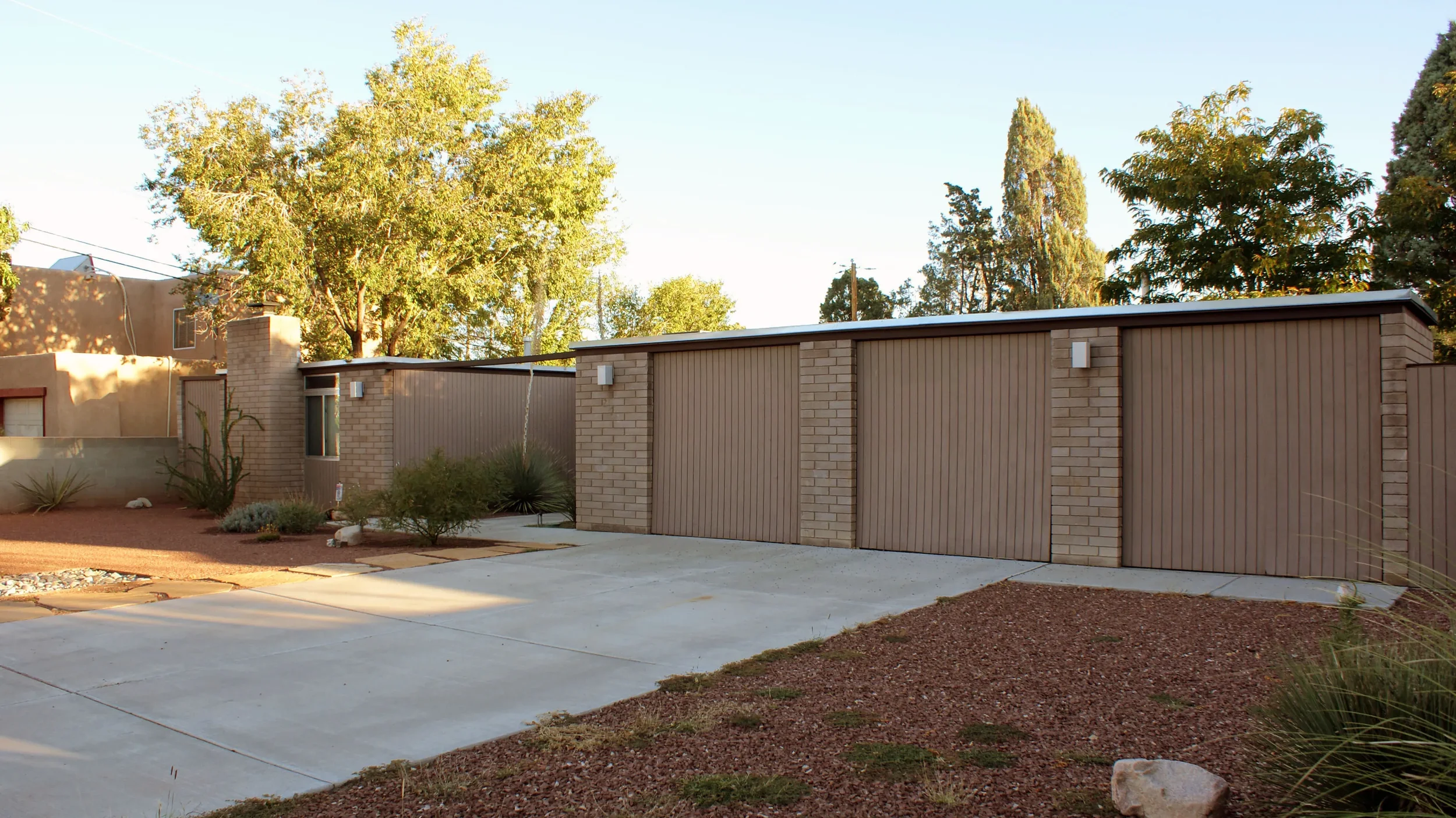 Photo of a modern residential house with a brick and metal exterior, a large driveway, and trees in the background.
