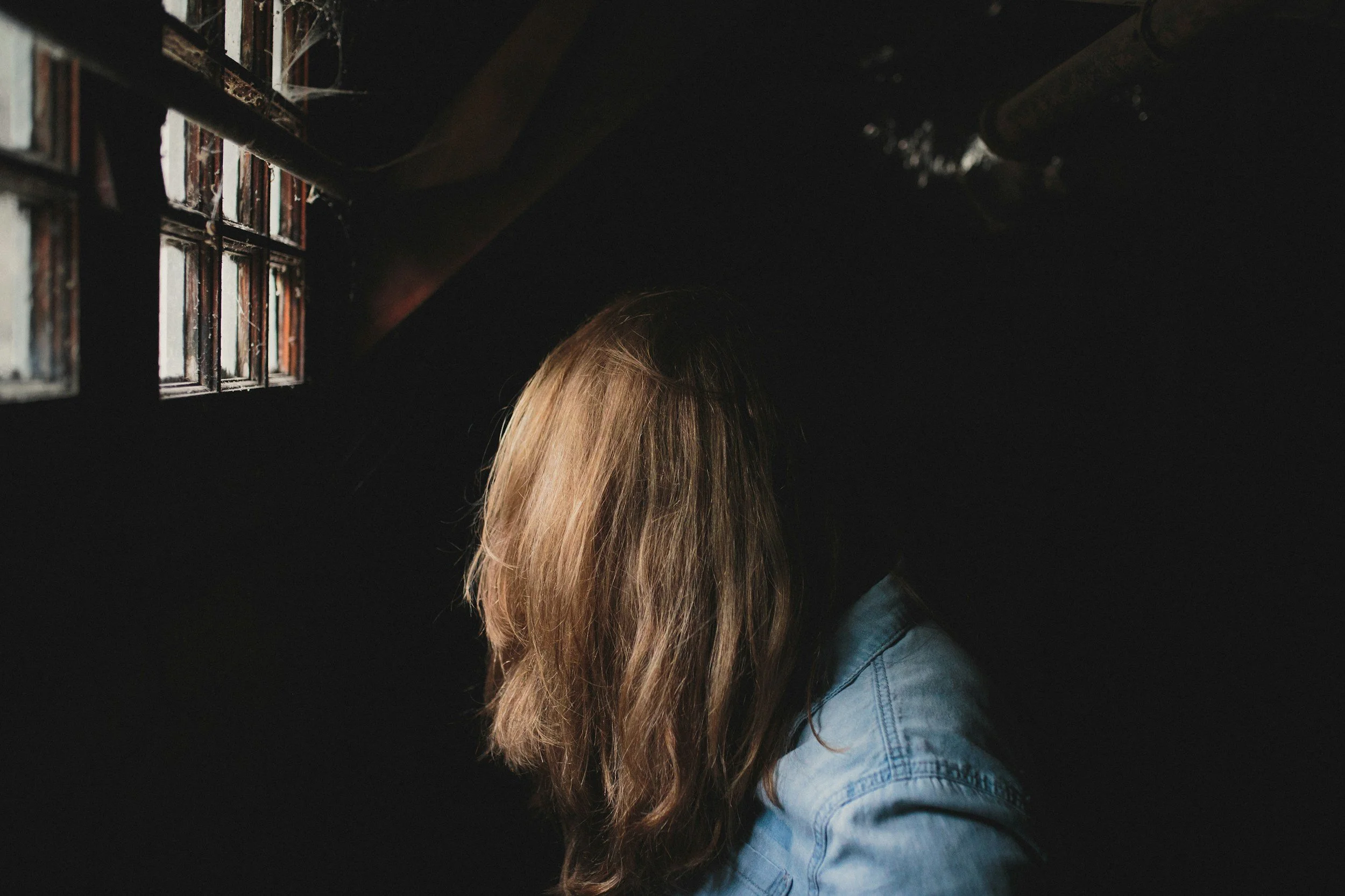 A woman covering her face with her hair in a darkened room