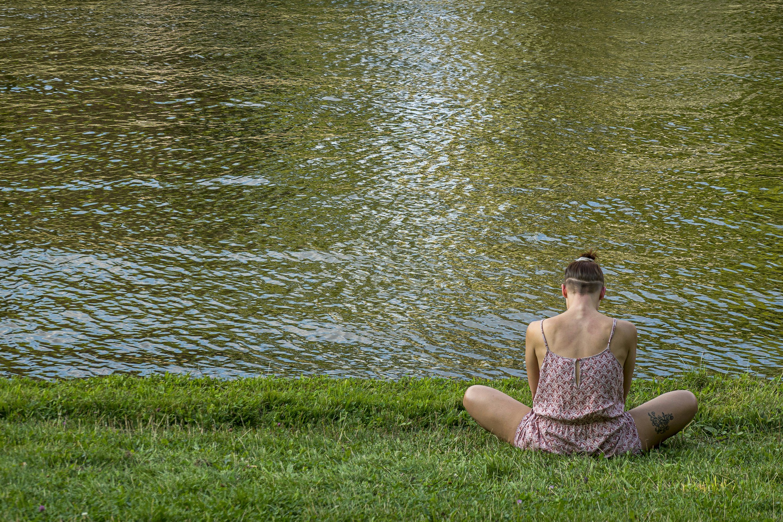 A women sat by a body of water focusing on her breath
