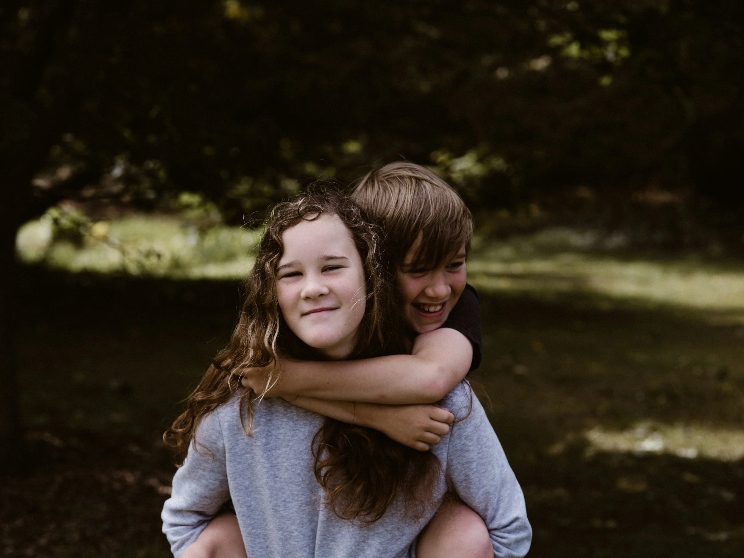 An older teen girl giving her younger preteen brother a piggy back in a park