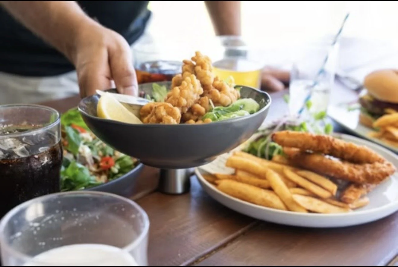 Bowl of fried chicken pieces with a cup of dipping sauce, lemon wedge, and leafy greens on a wooden table.