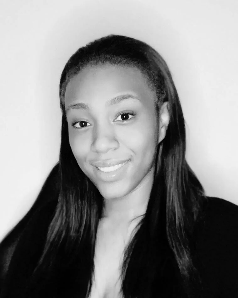 A smiling woman with long dark hair, wearing a dark top, is posing against a light-colored background.