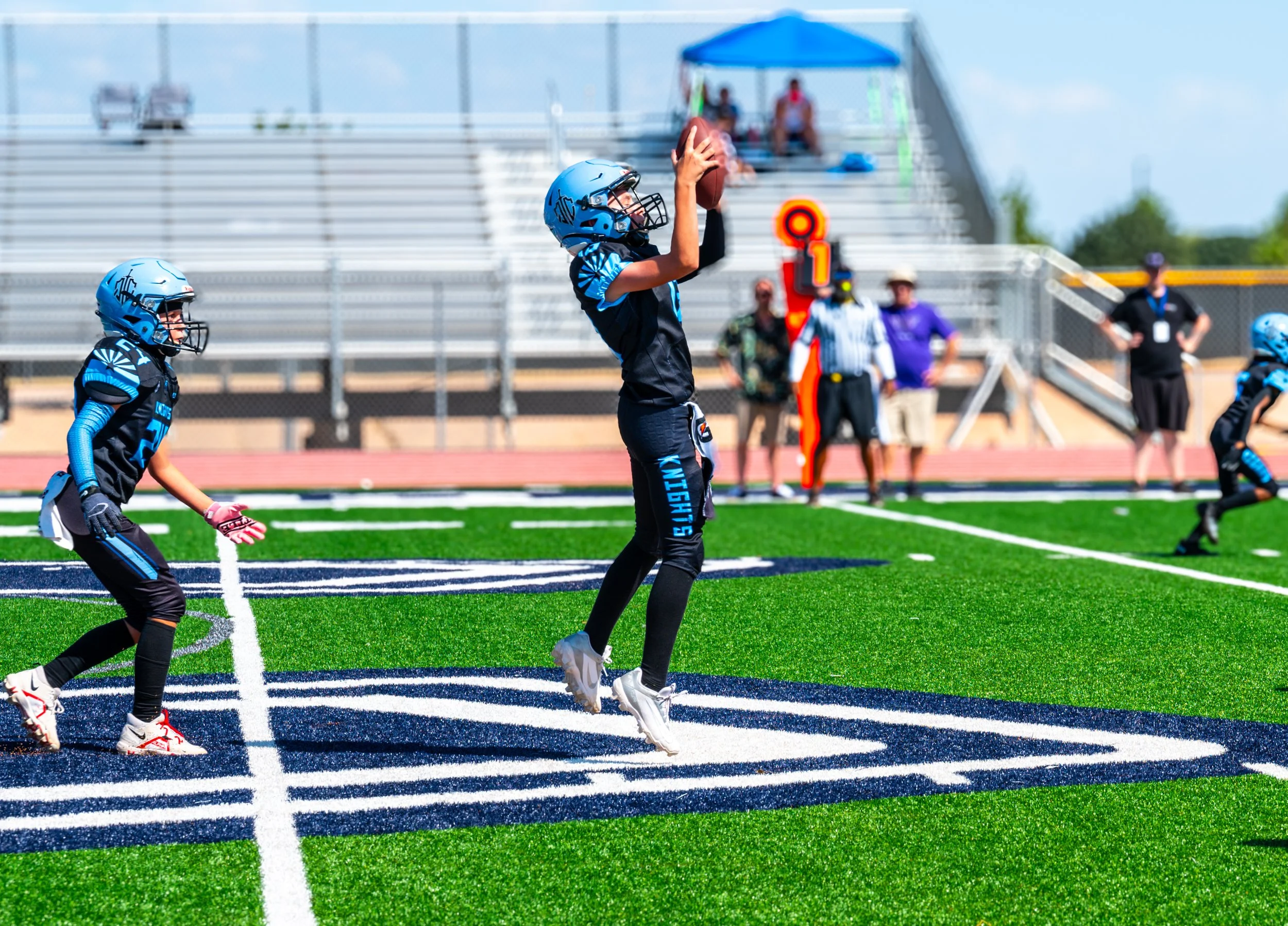 Young football player catching a football during a game on a synthetic turf field.